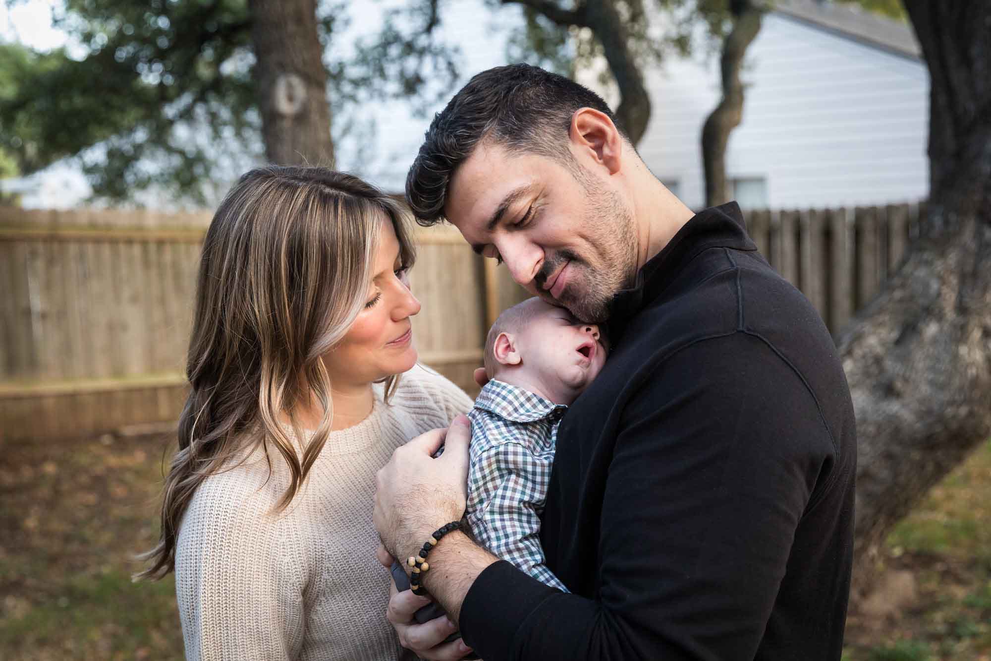 Mother and father looking down at newborn baby boy in backyard during an Austin newborn portrait session