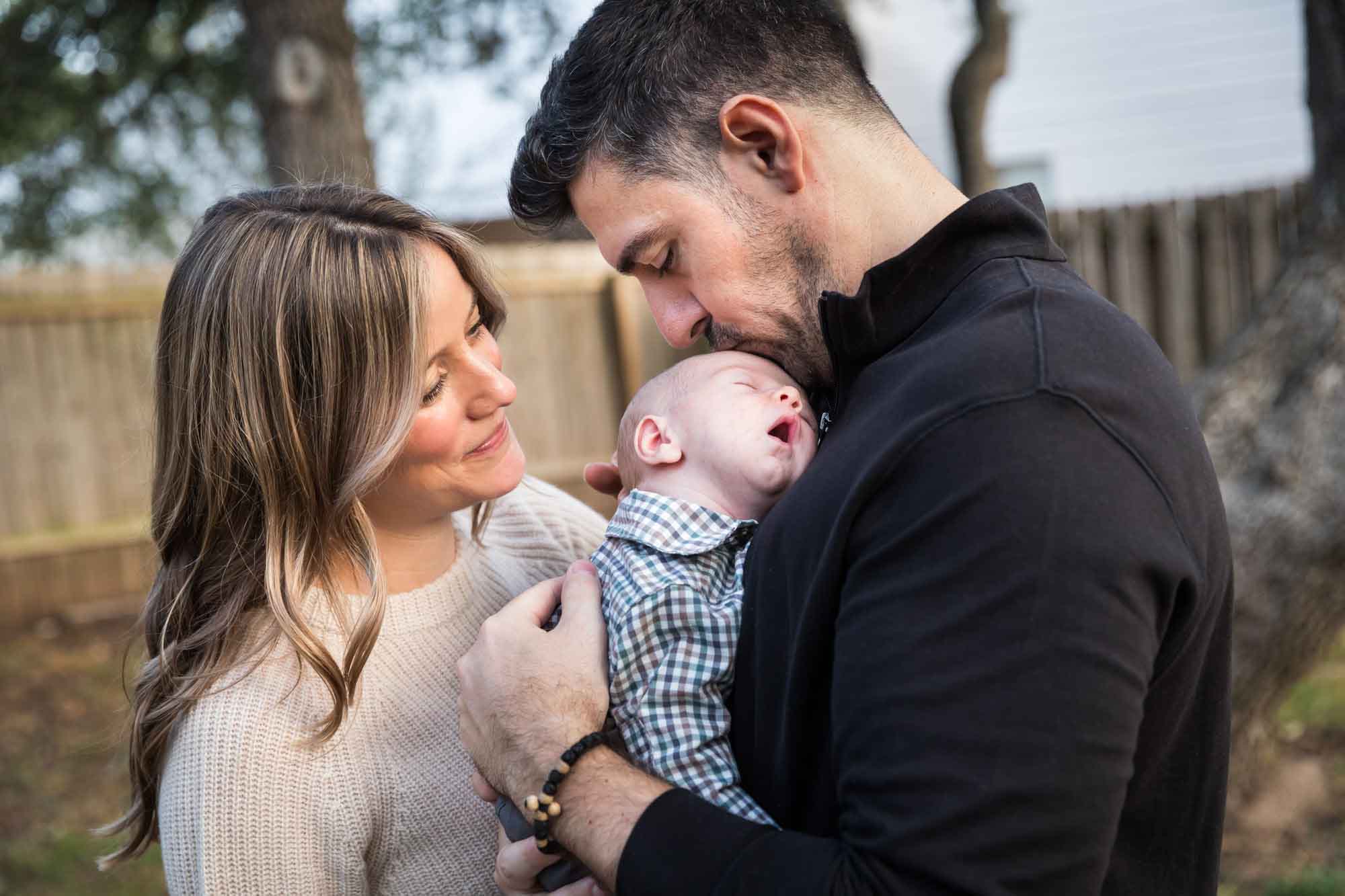 Mother and father looking down at newborn baby boy in backyard during an Austin newborn portrait session