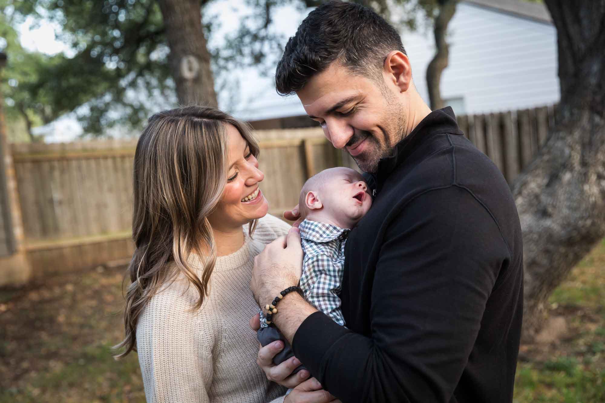 Mother and father looking down at newborn baby boy in backyard during an Austin newborn portrait session