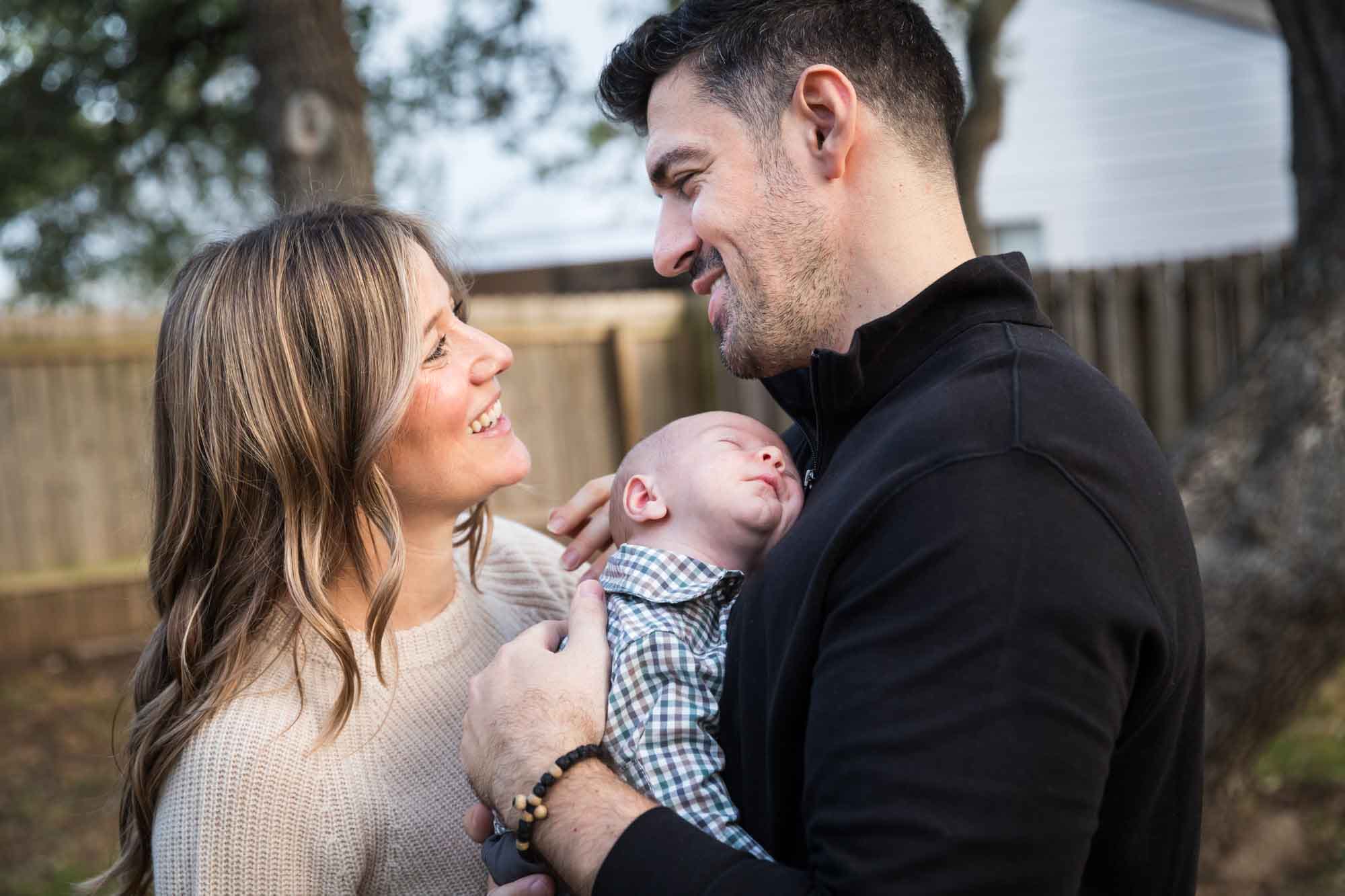 Mother and father looking at each other while holding newborn baby boy in backyard during an Austin newborn portrait session