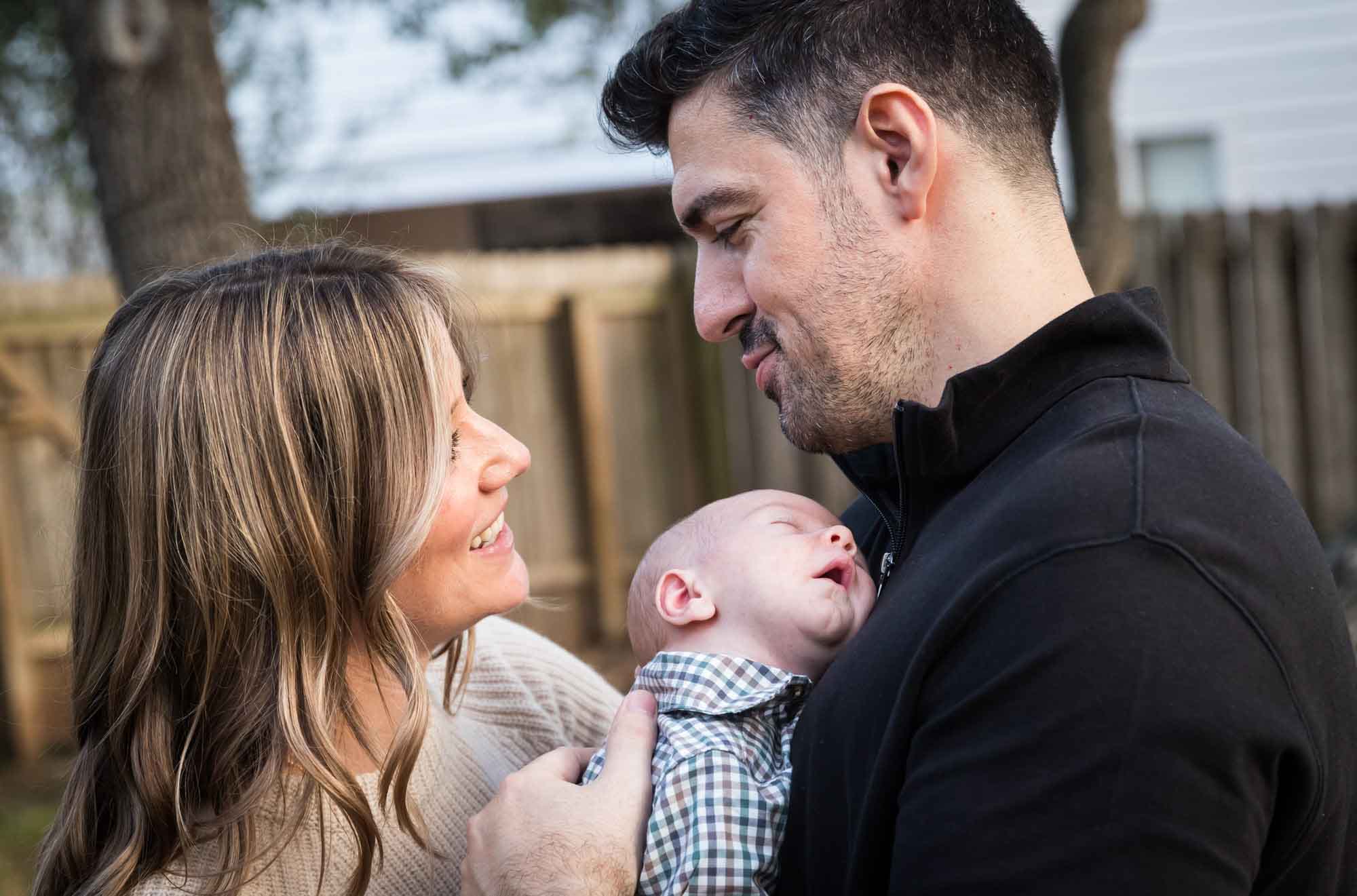 Mother and father looking at each other while holding newborn baby boy in backyard during an Austin newborn portrait session