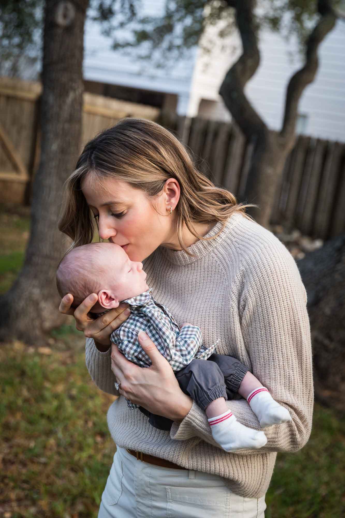 Mother kissing newborn baby boy in backyard during an Austin newborn portrait session