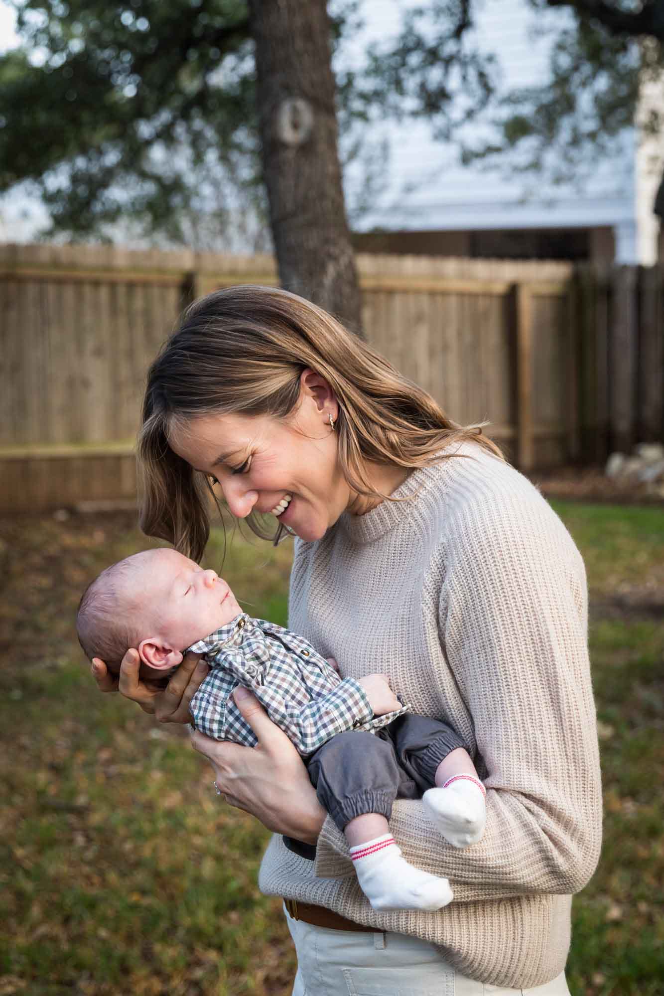 Mother looking down at newborn baby boy in backyard during an Austin newborn portrait session