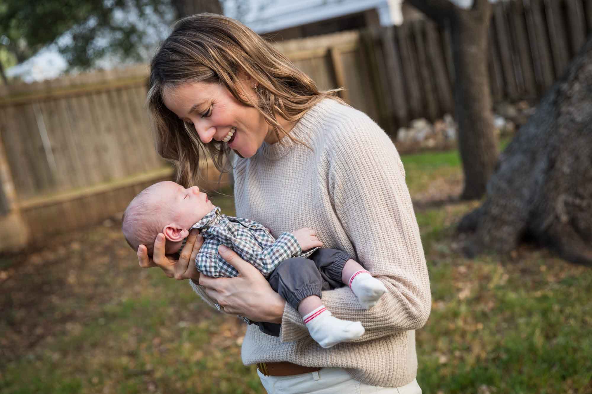 Mother looking down at newborn baby boy in backyard during an Austin newborn portrait session