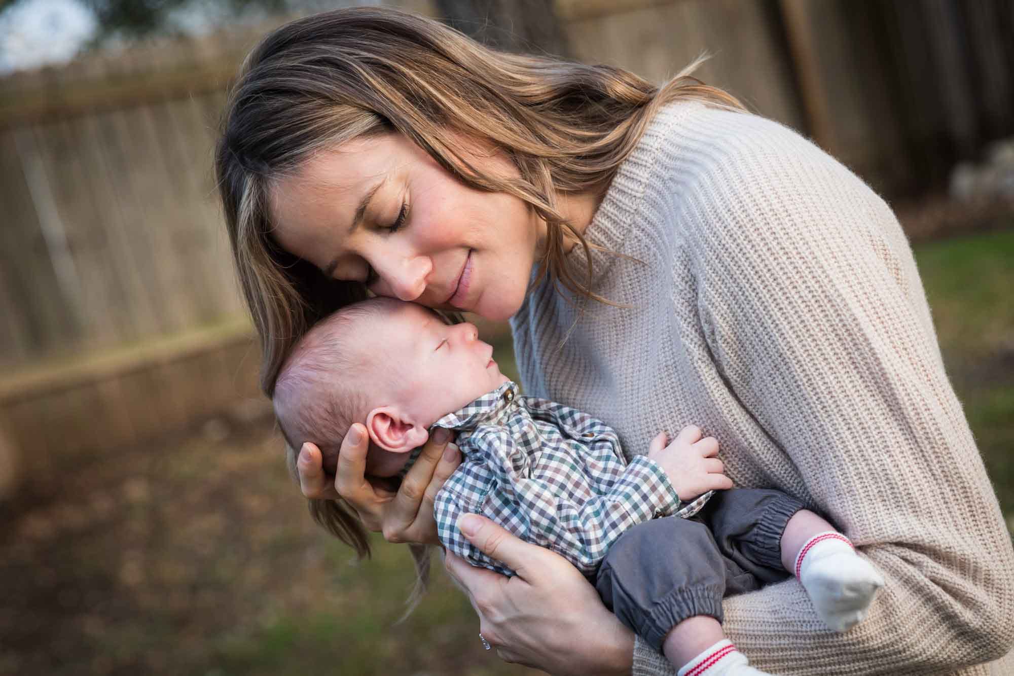 Mother holding newborn baby boy to cheek in backyard during an Austin newborn portrait session