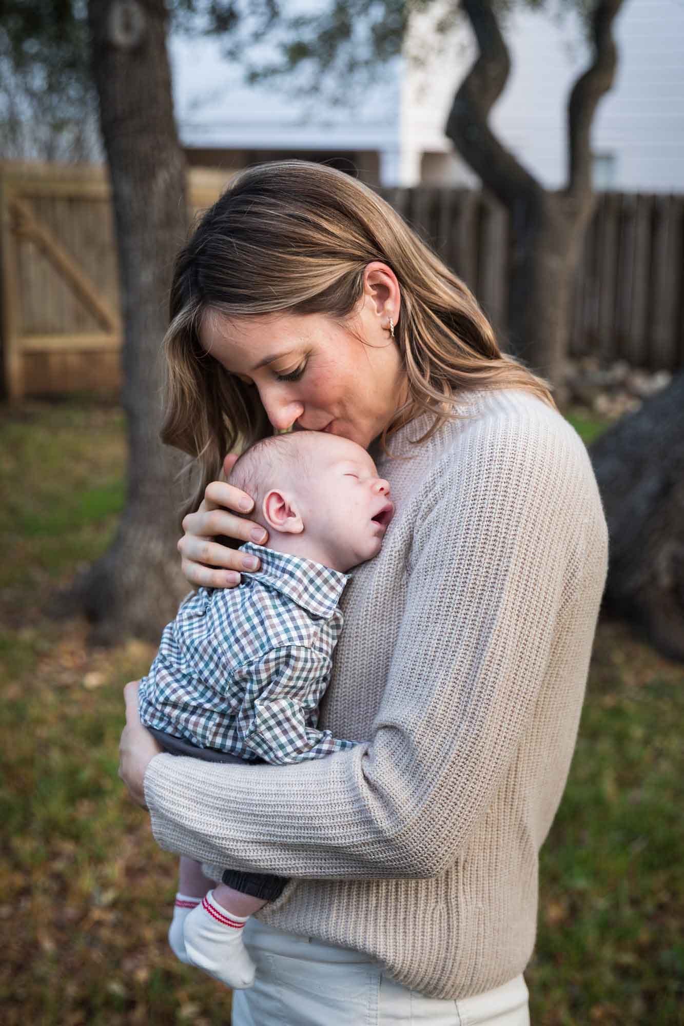 Mother kissing newborn baby boy in backyard during an Austin newborn portrait session