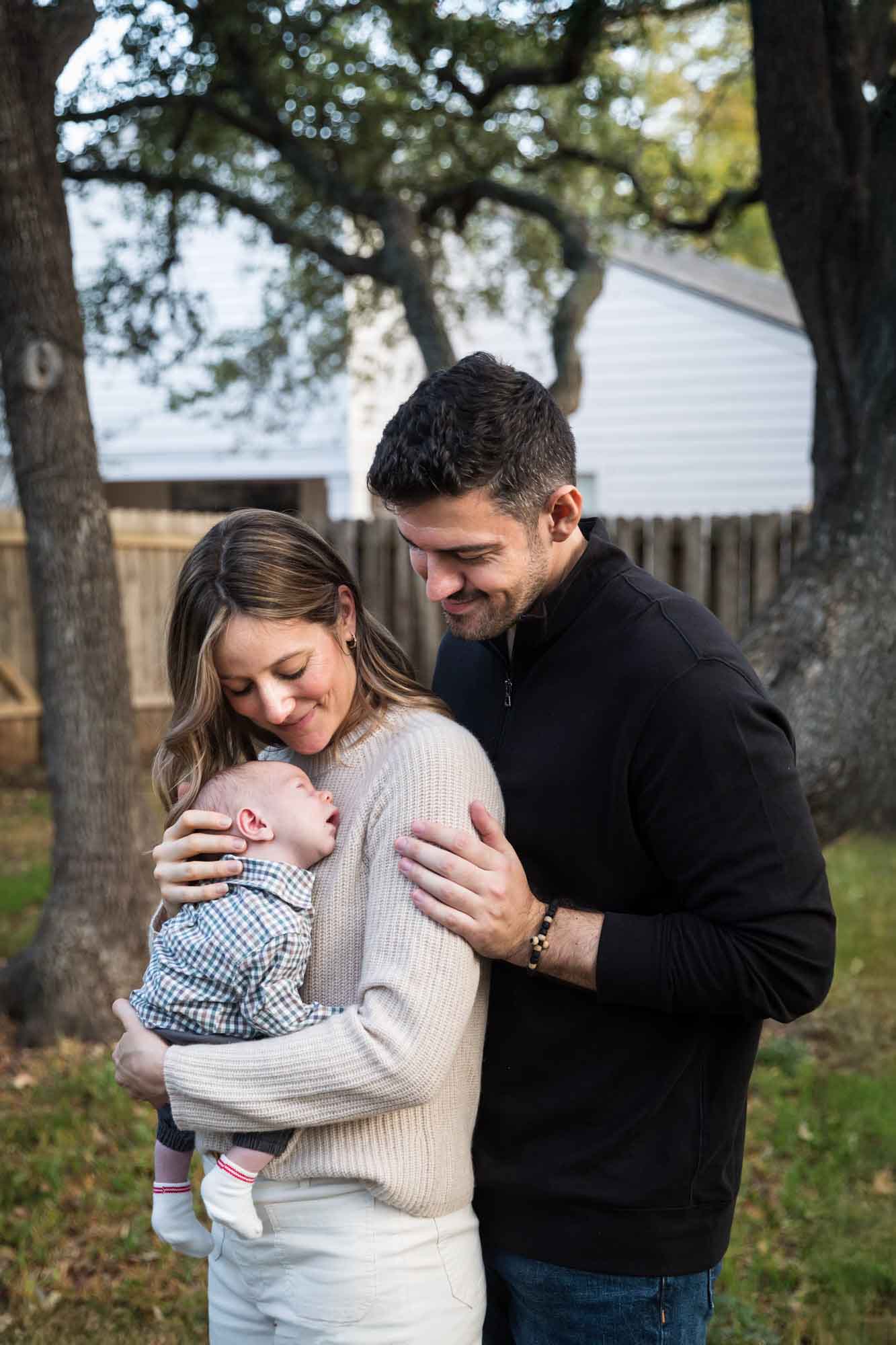 Mother and father looking down at newborn baby boy in backyard during an Austin newborn portrait session