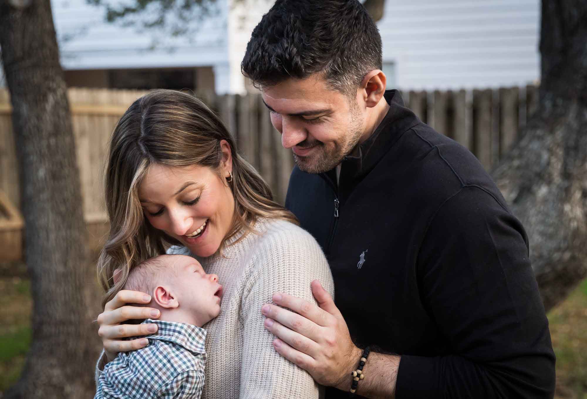 Mother and father looking down at newborn baby boy in backyard during an Austin newborn portrait session