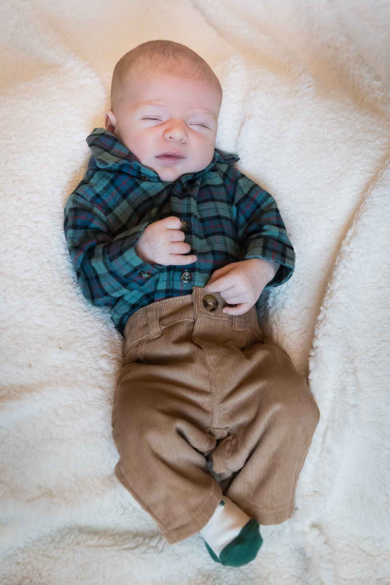 Baby boy wearing green and blue plaid shirt and brown corduroy pants resting on white, fleece blanket during an Austin newborn portrait session