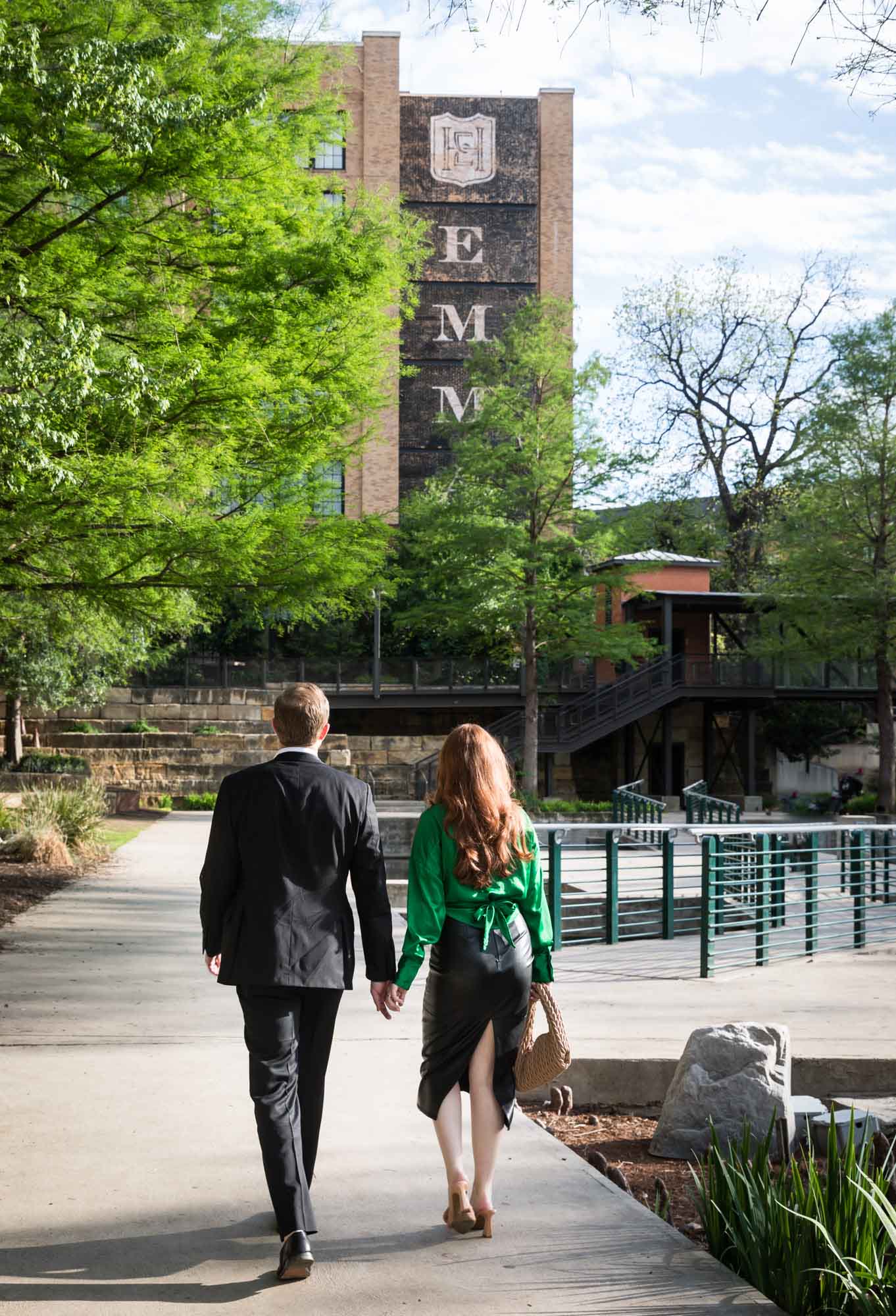 Man and woman walking hand in hand on sidewalk in front of Emma Hotel at the Historic Pearl beside Riverwalk