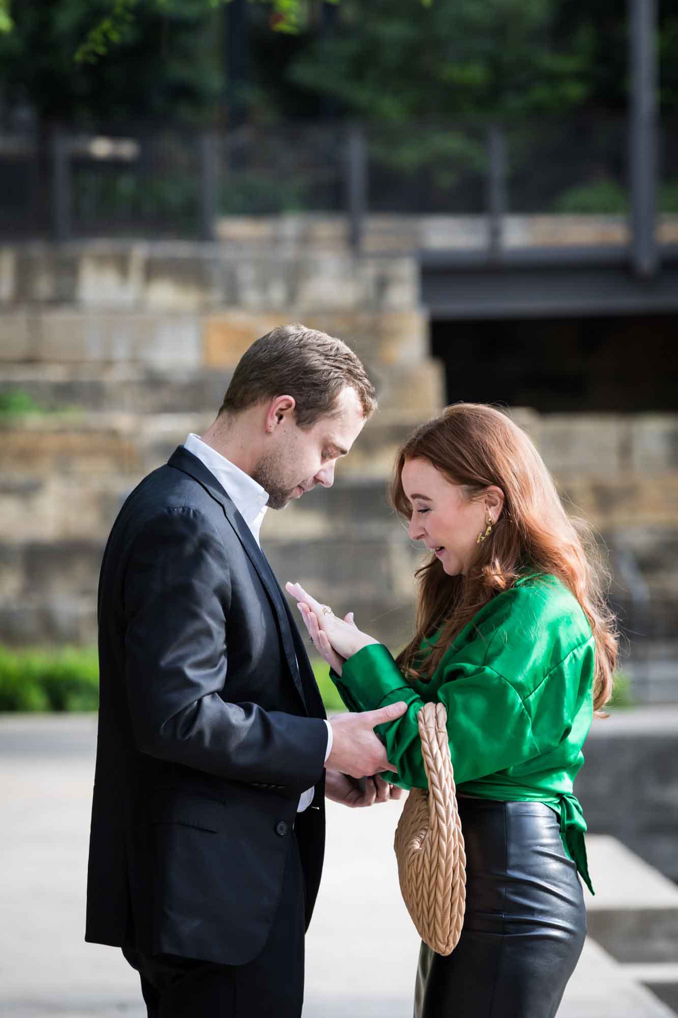Man wearing black suit standing in front of woman wearing green blouse on sidewalk in front of Emma Hotel beside Riverwalk during an Emma Hotel surprise proposal