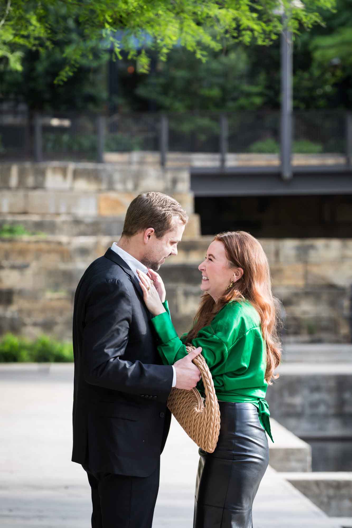Man wearing black suit standing in front of woman wearing green blouse on sidewalk in front of Emma Hotel beside Riverwalk during an Emma Hotel surprise proposal
