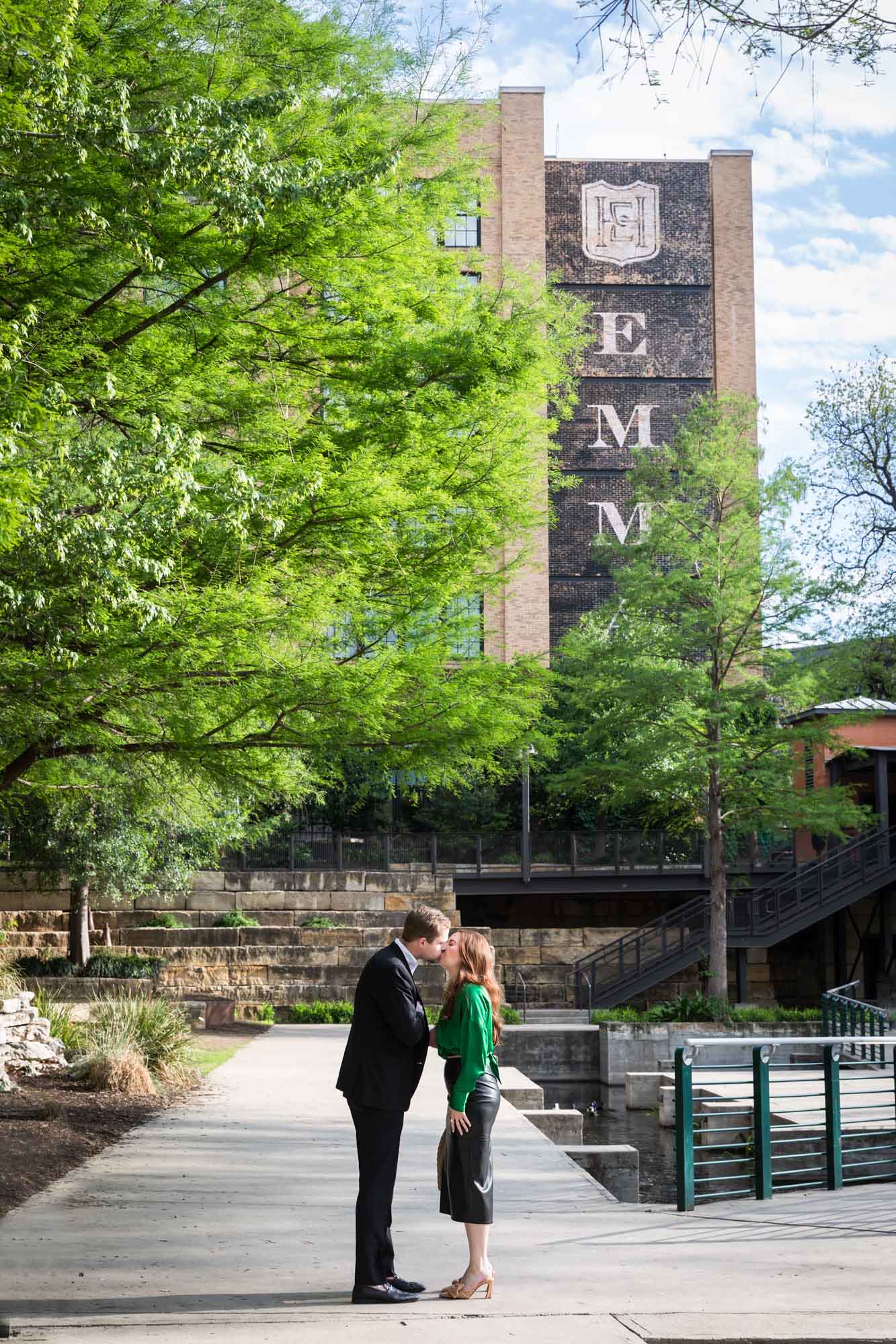Man and woman kissing on sidewalk in front of Emma Hotel beside Riverwalk during an Emma Hotel surprise proposal