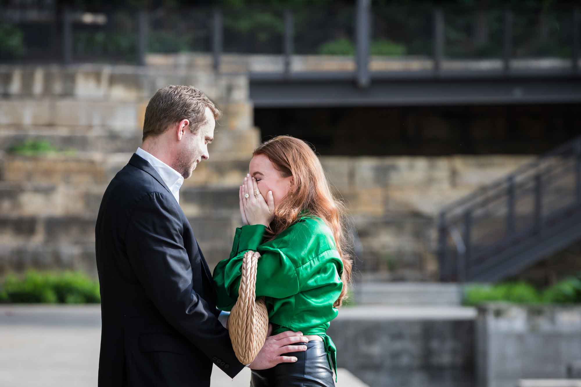Man wearing black suit standing in front of woman wearing green blouse on sidewalk in front of Emma Hotel beside Riverwalk during an Emma Hotel surprise proposal