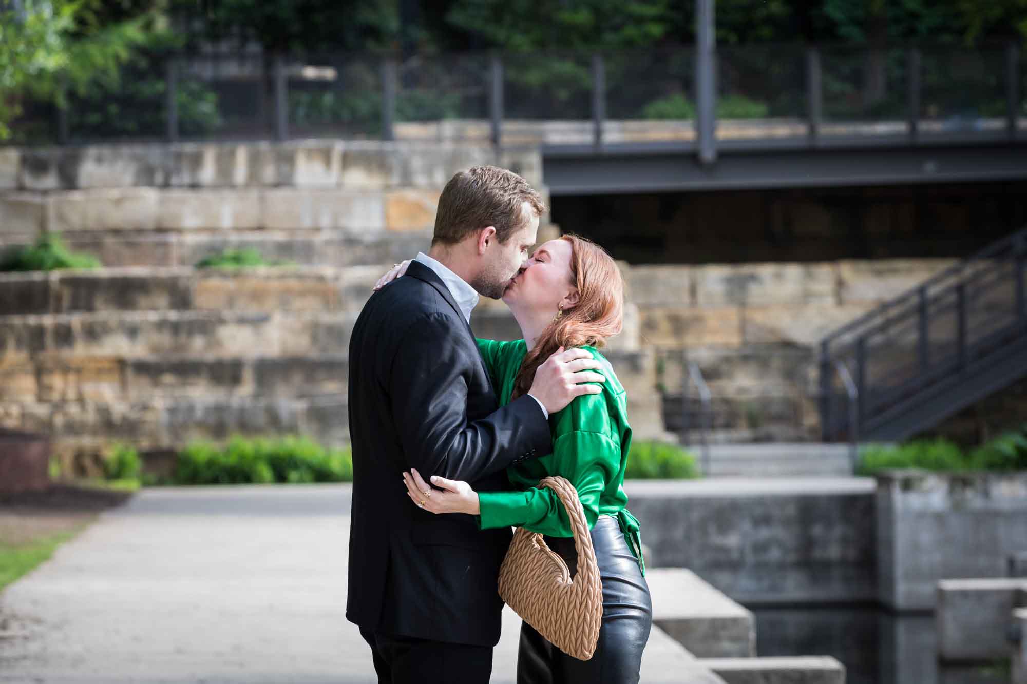 Man wearing black suit kissing woman wearing green blouse on sidewalk in front of Emma Hotel beside Riverwalk during an Emma Hotel surprise proposal