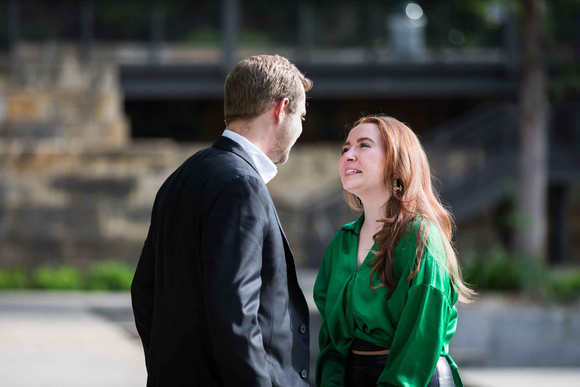 Man wearing black suit standing in front of woman wearing green blouse on sidewalk in front of Emma Hotel beside Riverwalk during an Emma Hotel surprise proposal