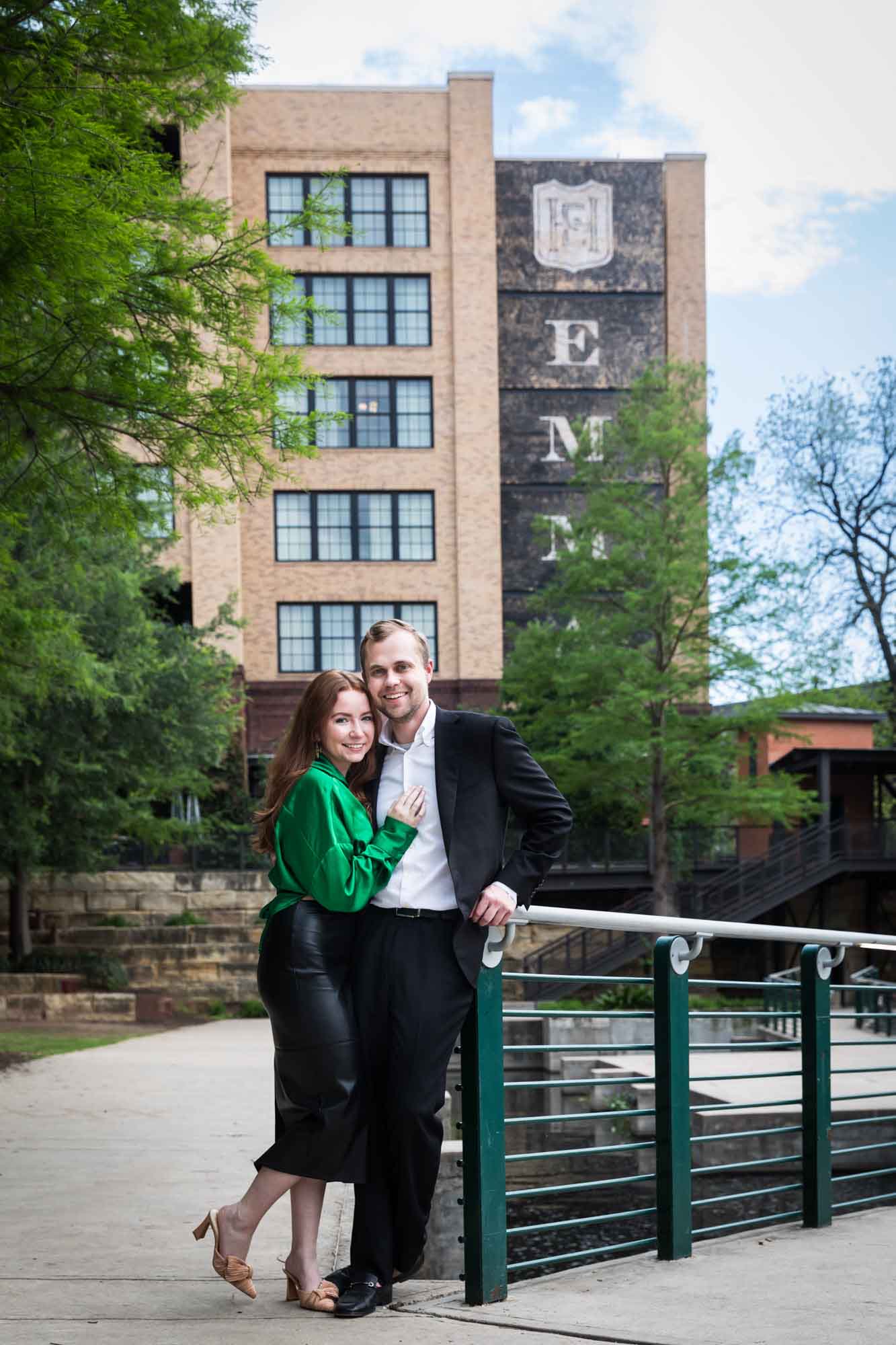 Man wearing black suit standing with woman wearing green blouse in front of Emma Hotel during an Emma Hotel surprise proposal