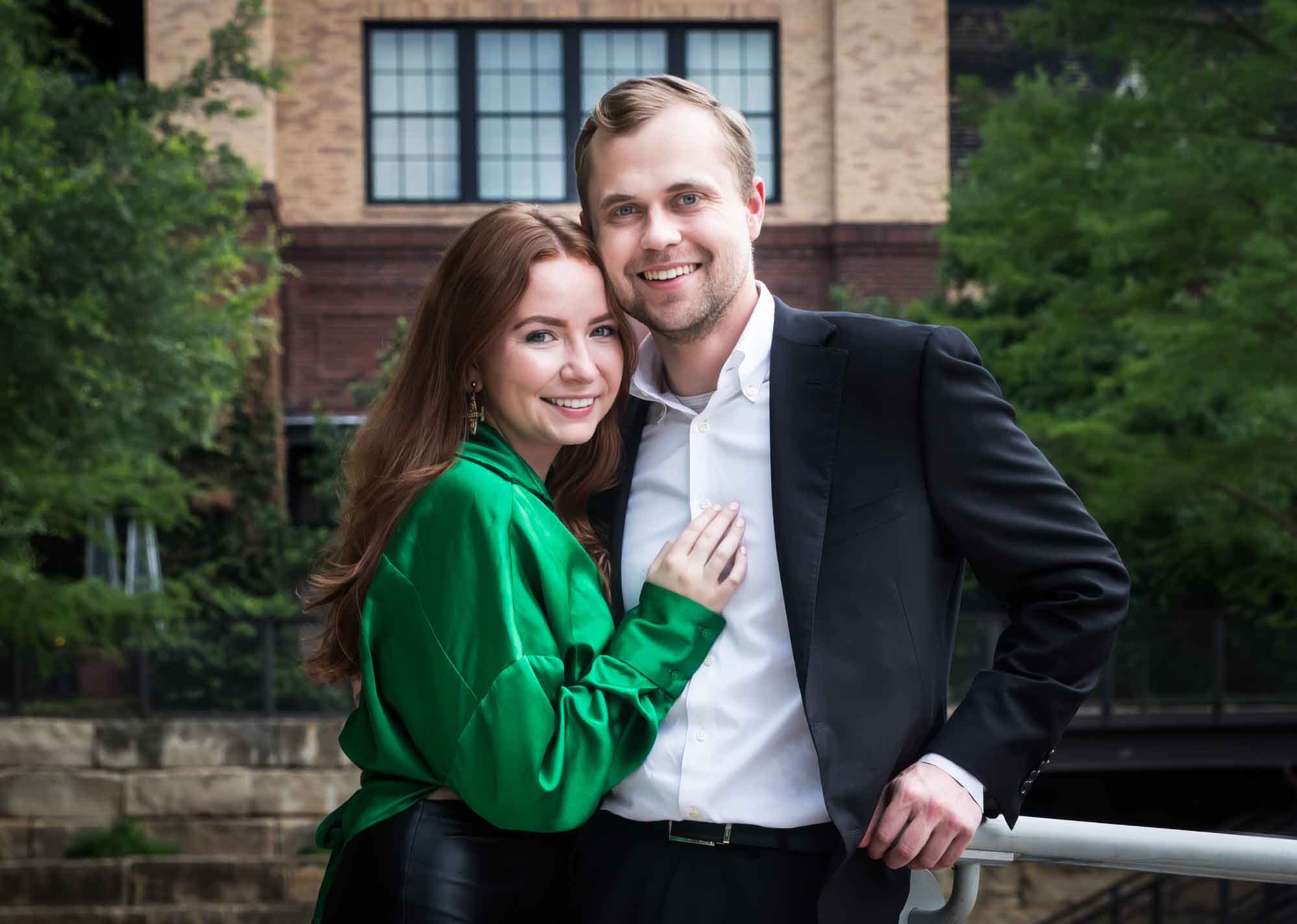 Man wearing black suit standing with woman wearing green blouse in front of Emma Hotel during an Emma Hotel surprise proposal