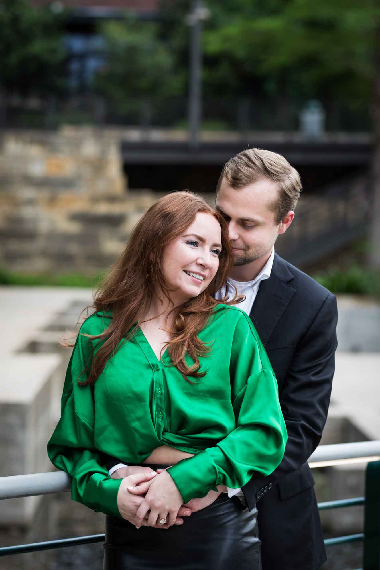 Man wearing black suit standing with woman wearing green blouse in front of Emma Hotel along railing during an Emma Hotel surprise proposal