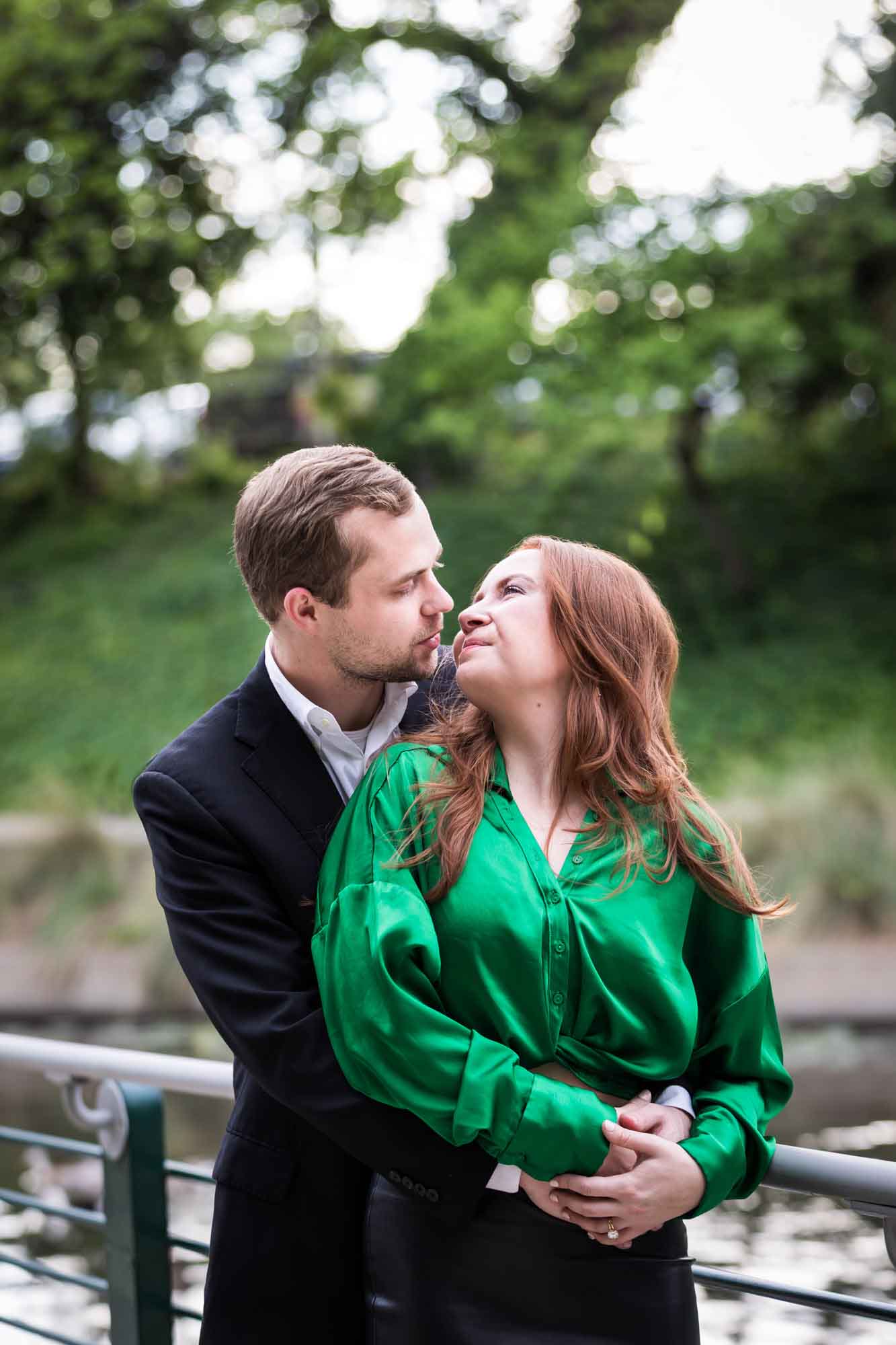 Man wearing black suit standing with woman wearing green blouse along railing beside Riverwalk during an Emma Hotel surprise proposal