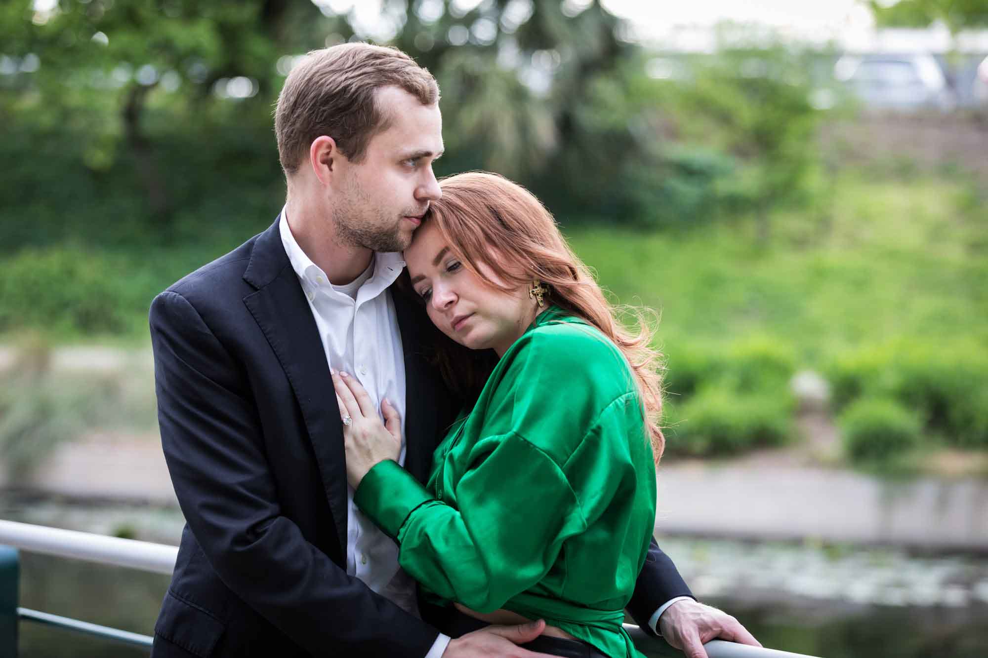 Man wearing black suit standing with woman wearing green blouse along railing beside Riverwalk during an Emma Hotel surprise proposal