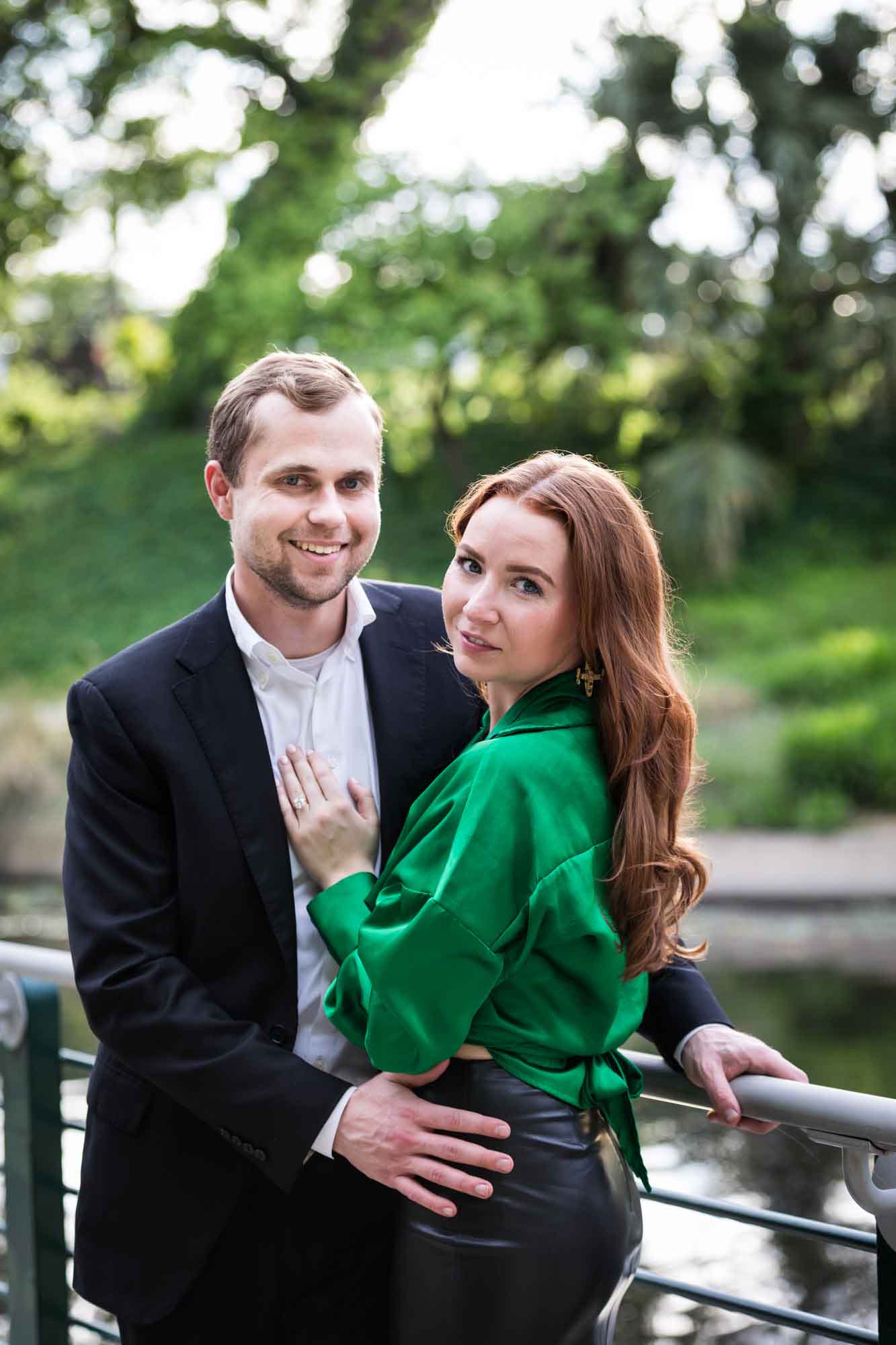 Man wearing black suit standing with woman wearing green blouse along railing beside Riverwalk during an Emma Hotel surprise proposal