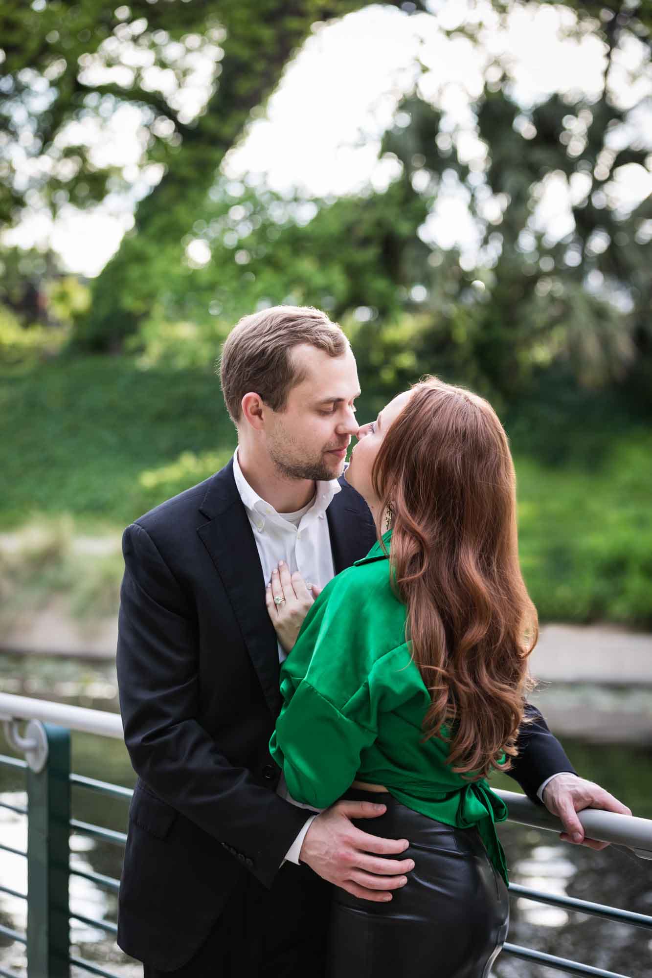 Man wearing black suit standing with woman wearing green blouse along railing beside Riverwalk during an Emma Hotel surprise proposal