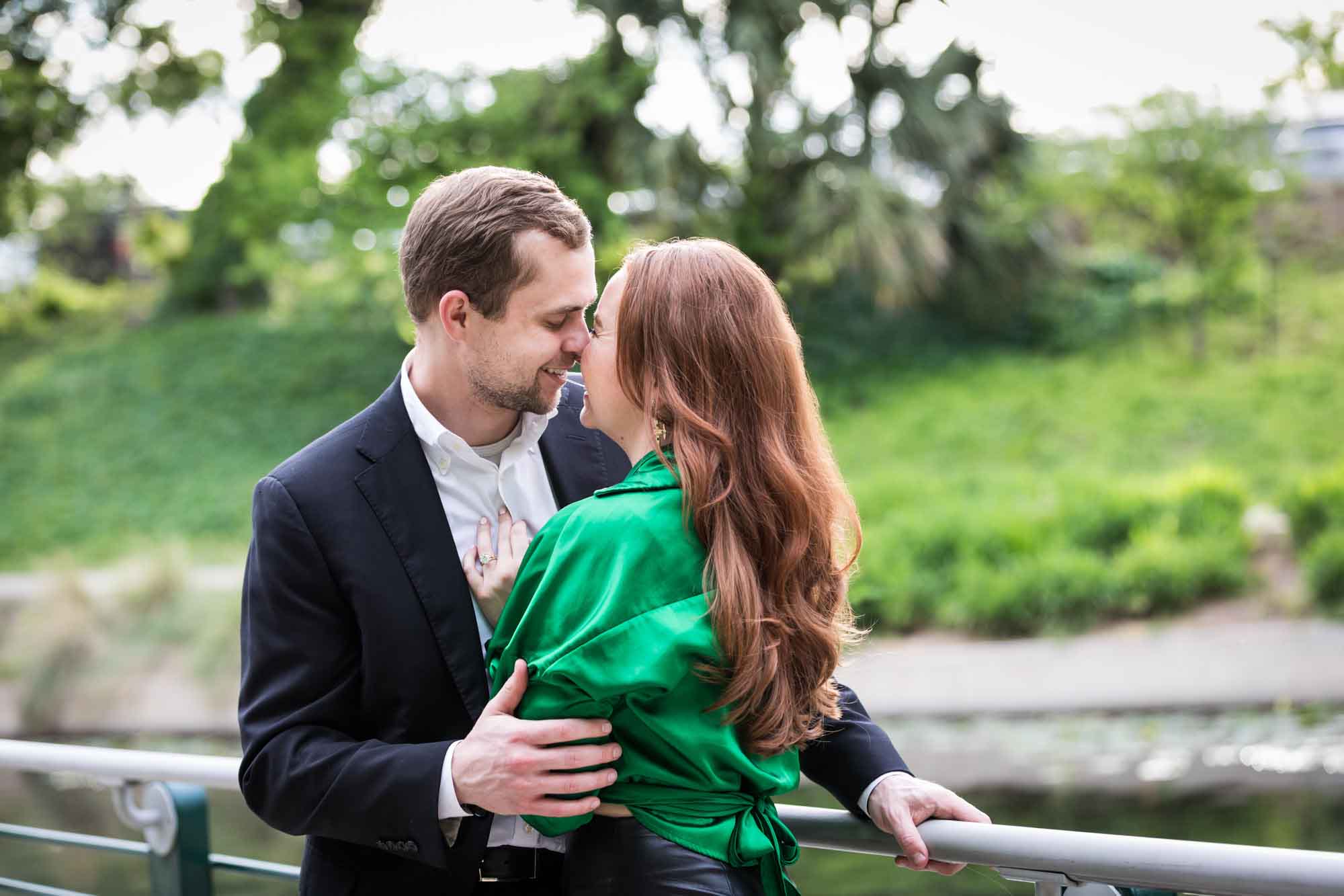 Man wearing black suit standing with woman wearing green blouse along railing beside Riverwalk during an Emma Hotel surprise proposal