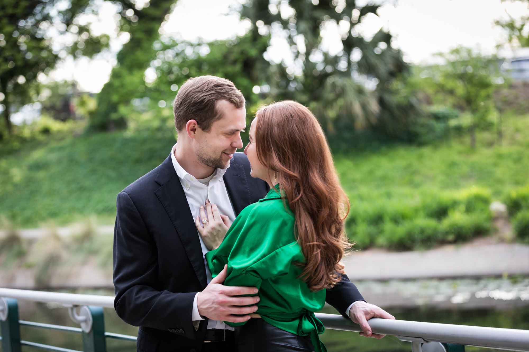 Man wearing black suit standing with woman wearing green blouse along railing beside Riverwalk during an Emma Hotel surprise proposal