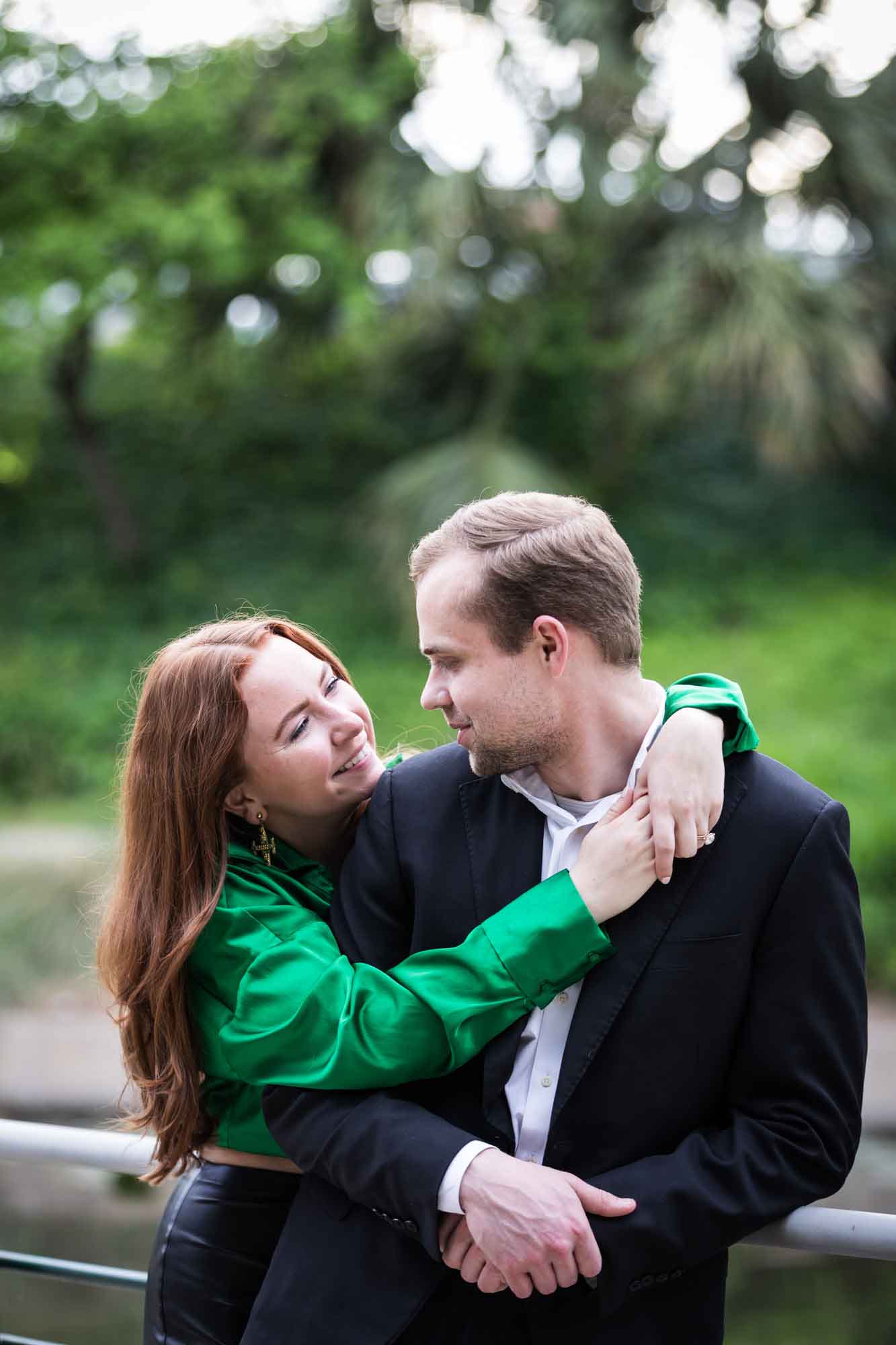 Man wearing black suit being hugged by woman wearing green blouse along railing beside Riverwalk during an Emma Hotel proposal