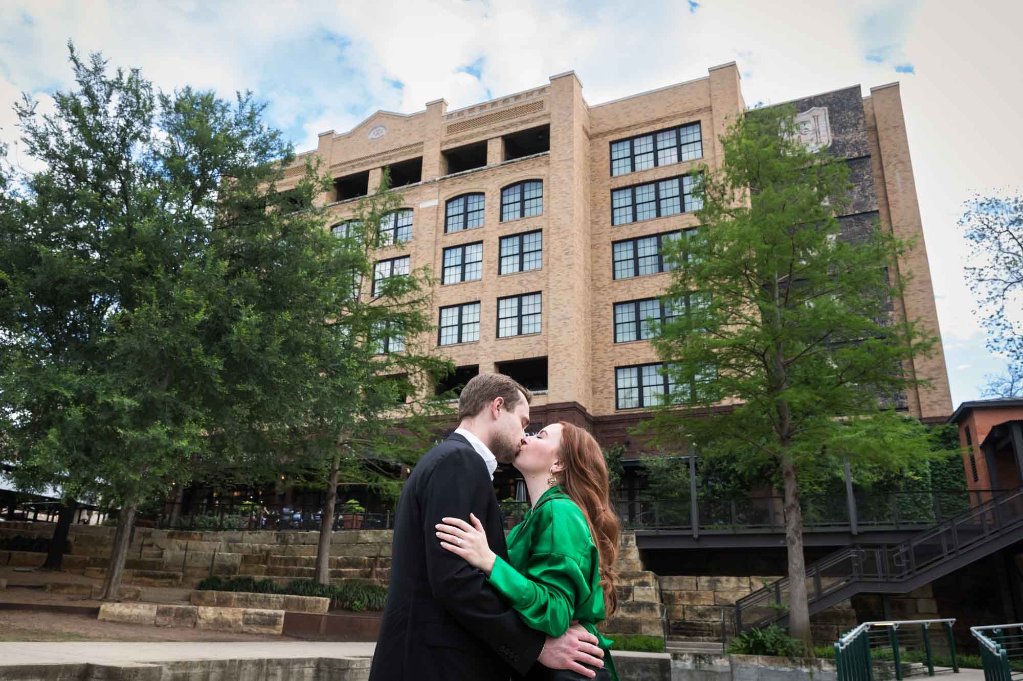Man wearing black suit kissing woman wearing green blouse in front of Emma Hotel during an Emma Hotel proposal