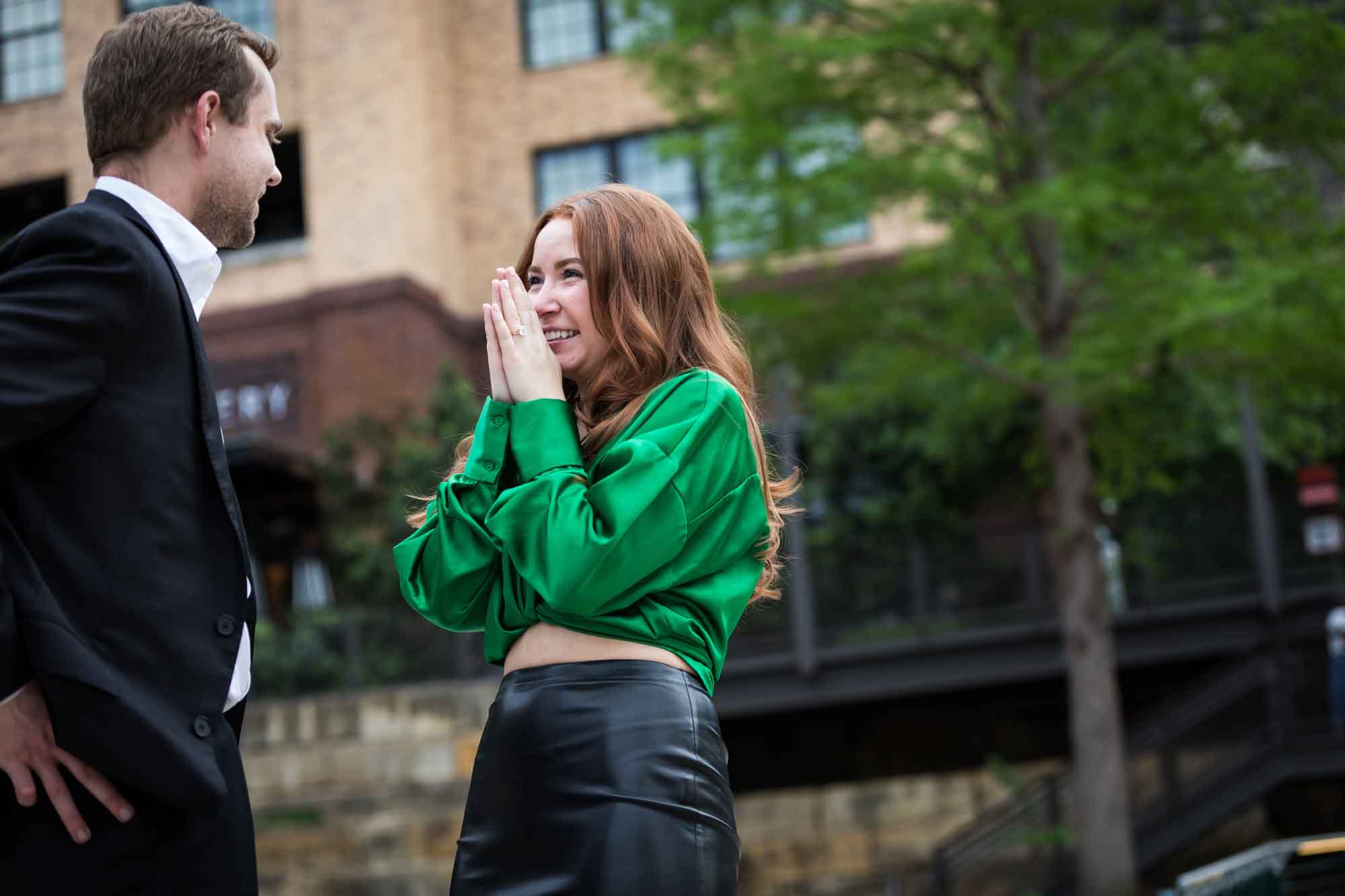 Man wearing black suit standing with laughing woman wearing green blouse in front of Emma Hotel during an Emma Hotel proposal