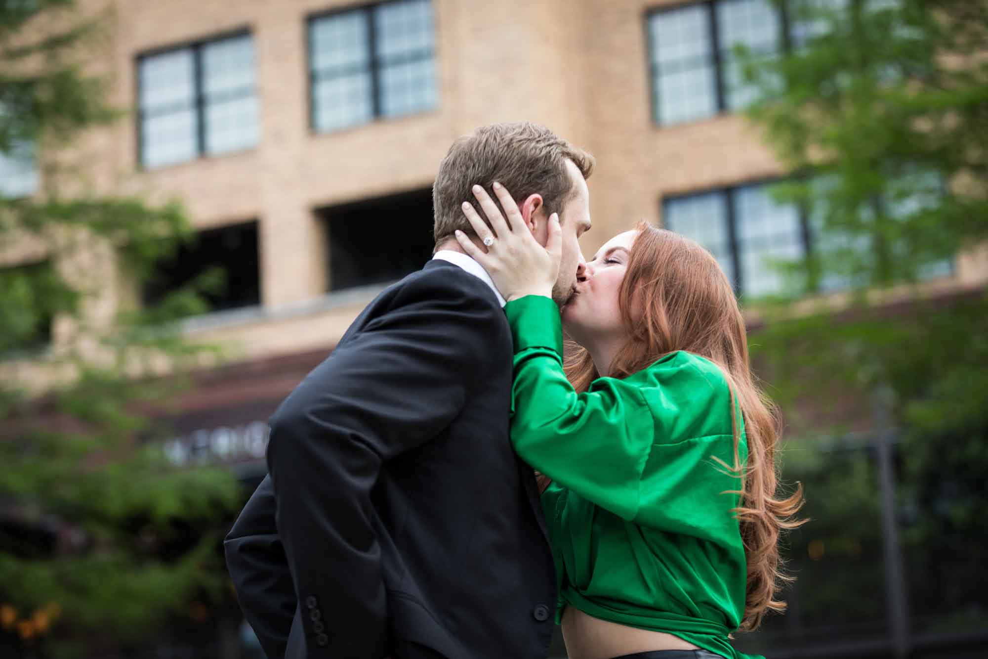 Man wearing black suit being kissed by woman wearing green blouse in front of Emma Hotel during an Emma Hotel proposal