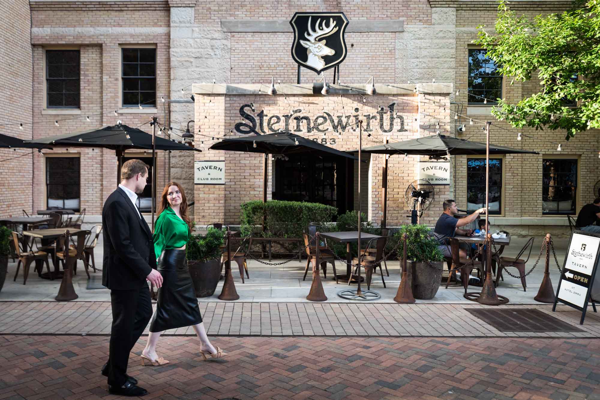 Man and woman holding hands walking past Sternewirth Bar on cobblestone street at the Pearl during an Emma Hotel engagement photo shoot