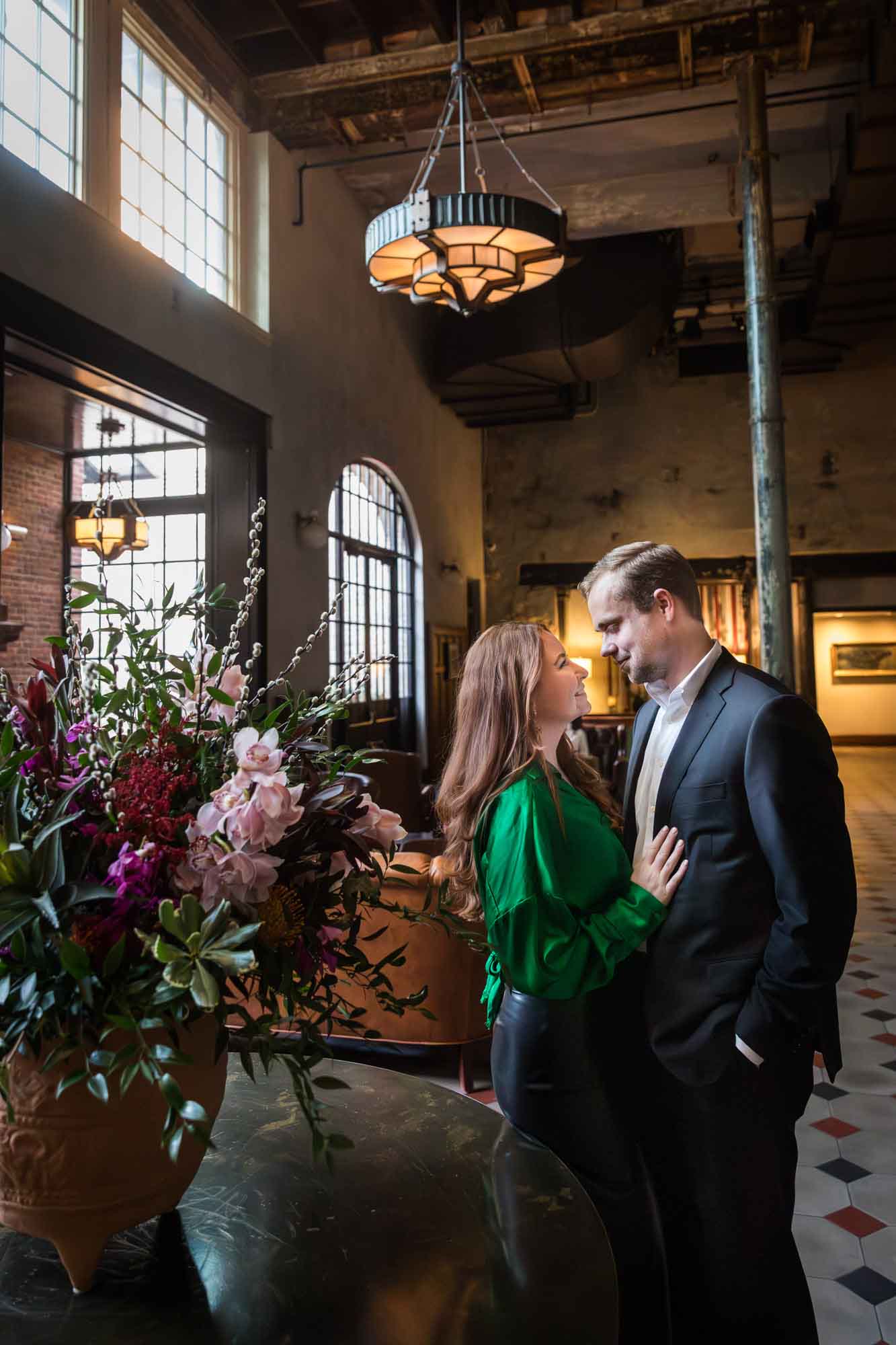 Man and woman hugging in front of table with flower bouquet in Emma Hotel lobby during an Emma Hotel engagement photo shoot