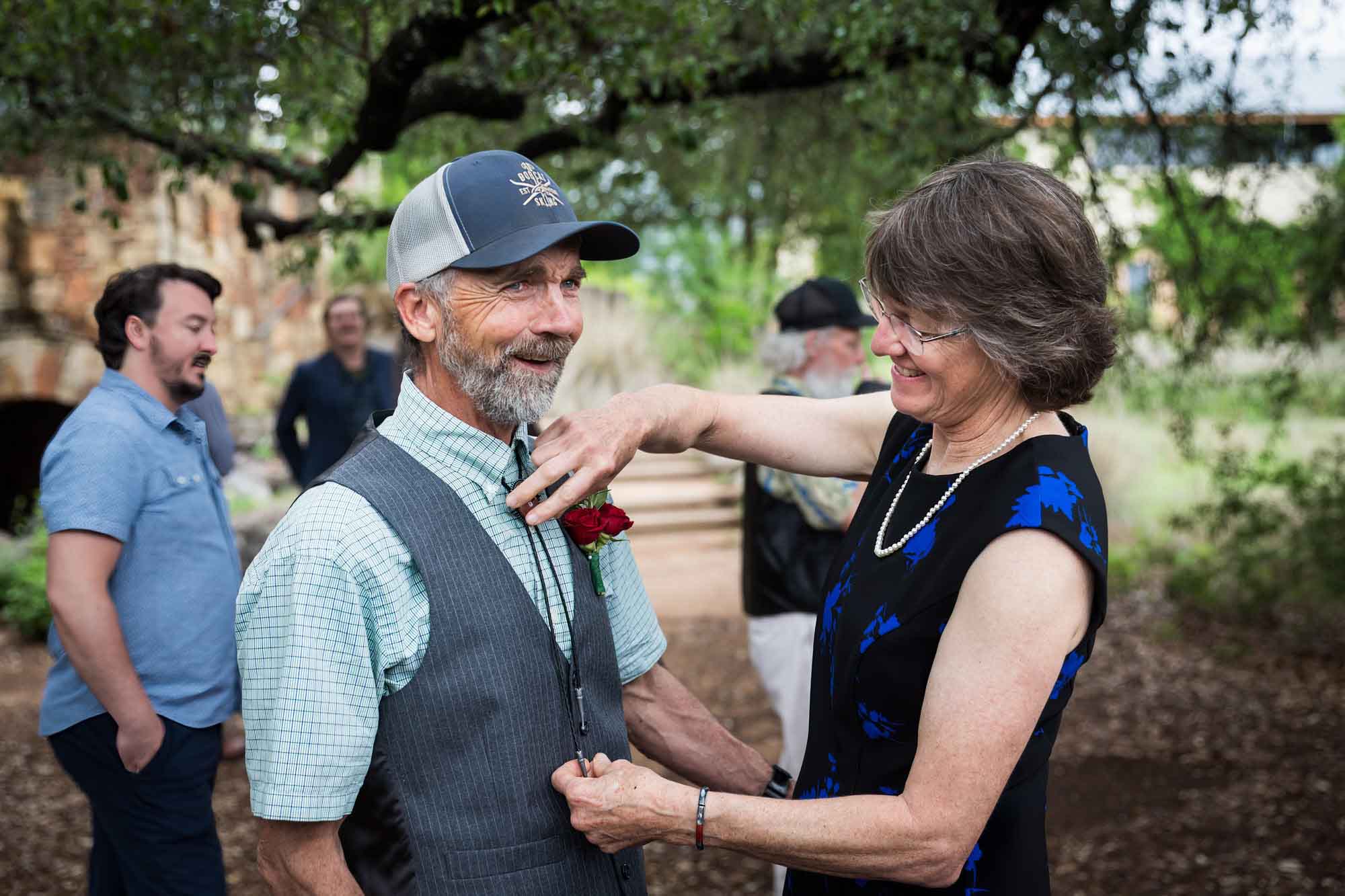 Woman adjusting bolero tie on man wearing vest and ballcap during a Lady Bird Johnson Wildflower Center wedding