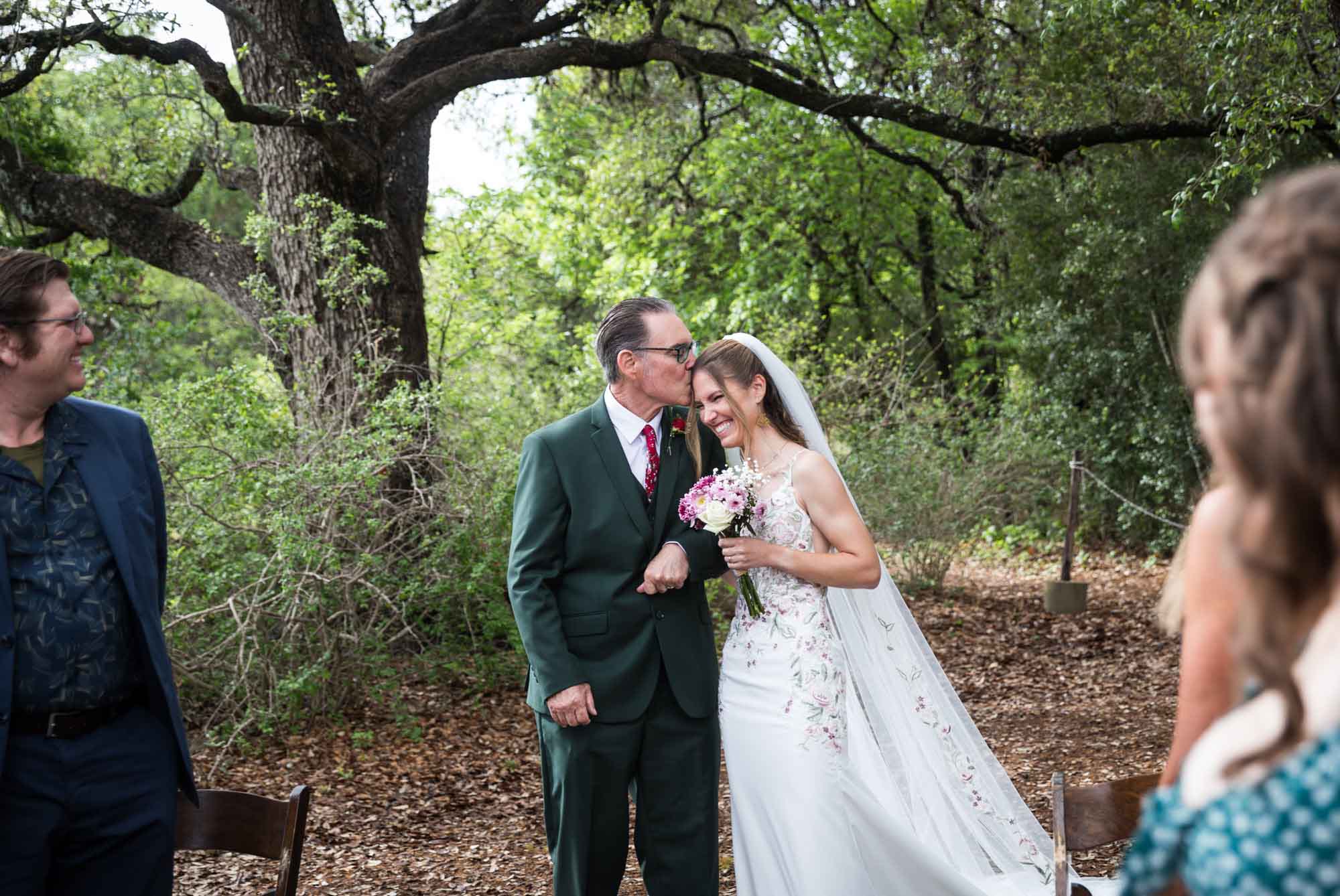 Father kissing bride on the head in front of guests during ceremony during a Lady Bird Johnson Wildflower Center wedding