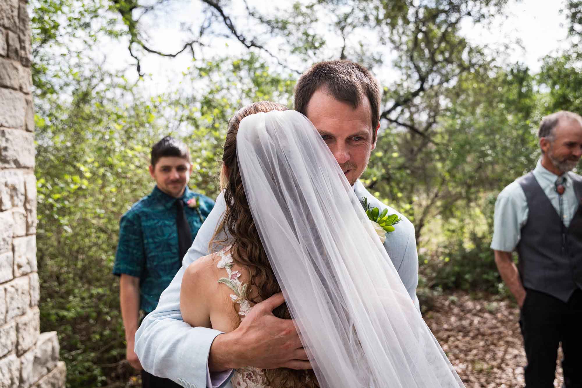 Groom hugging bride wearing veil during ceremony during a Lady Bird Johnson Wildflower Center wedding