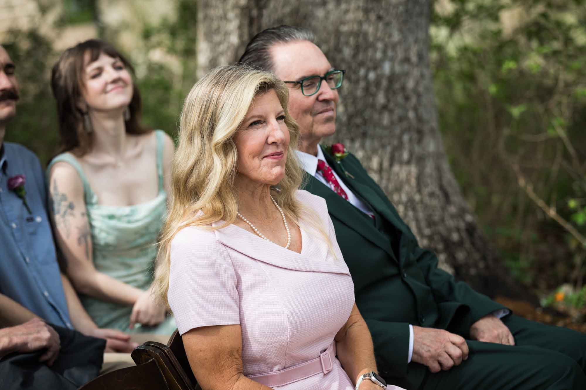 Mother of bride wearing pink dress and father of bride wearing green suit seated during ceremony during a Lady Bird Johnson Wildflower Center wedding