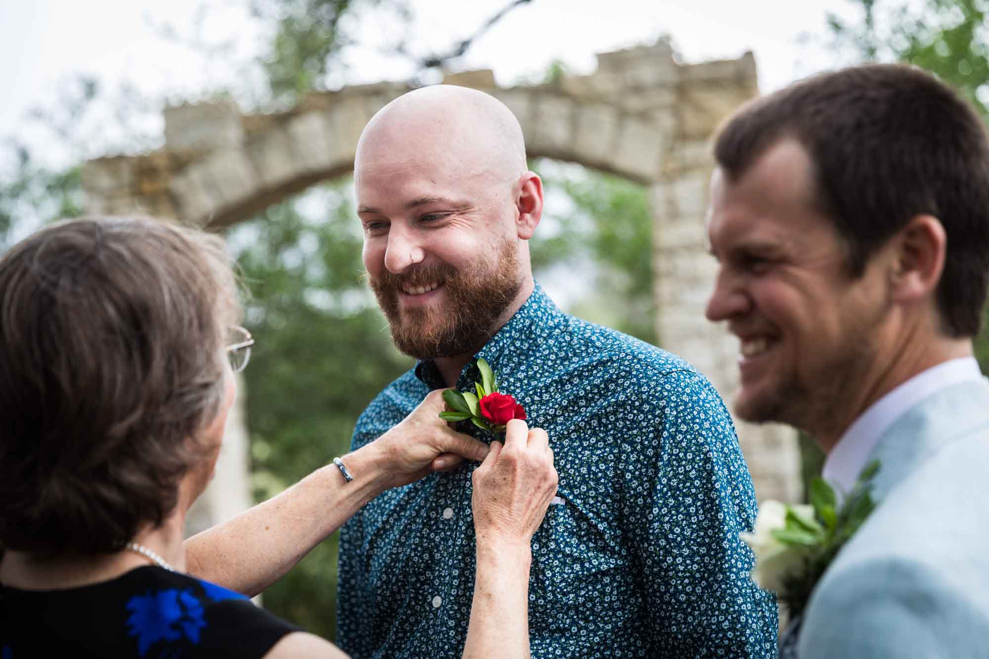 Woman pinning flower to bald man's blue shirt during a Lady Bird Johnson Wildflower Center wedding