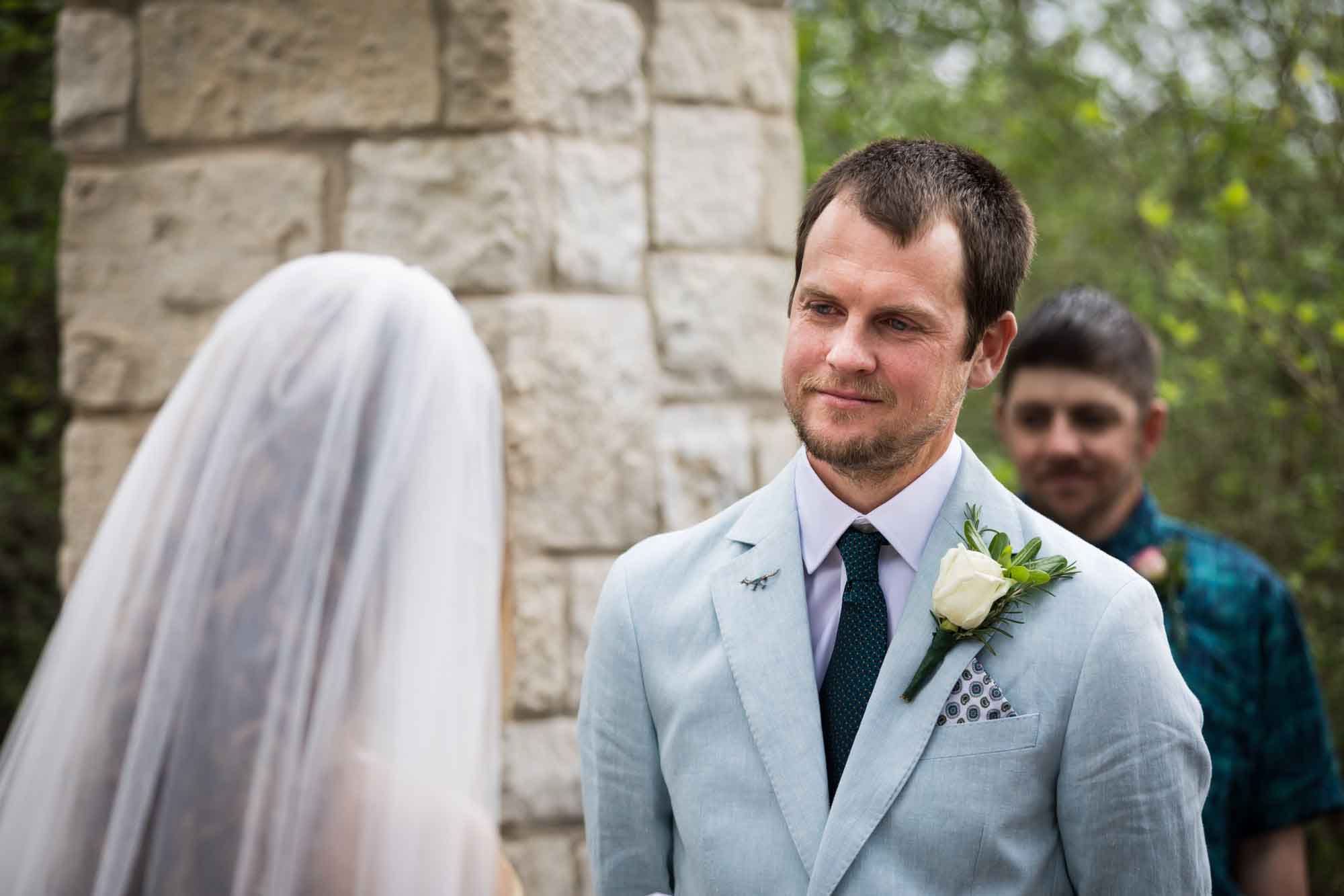 Groom wearing light blue blazer with tears on his face standing in front of Cecille's Arch during a Lady Bird Johnson Wildflower Center wedding