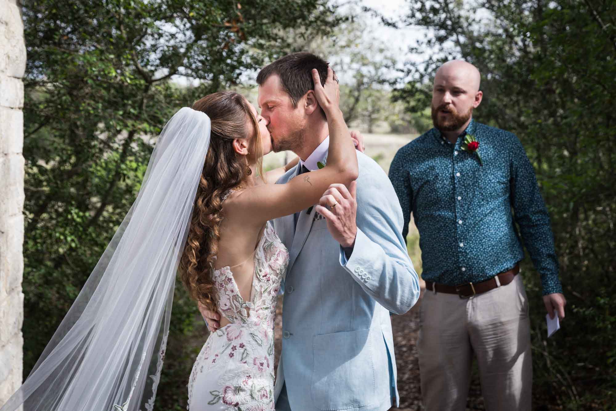 Bride and groom kissing in front of officiant after ceremony during a Lady Bird Johnson Wildflower Center wedding