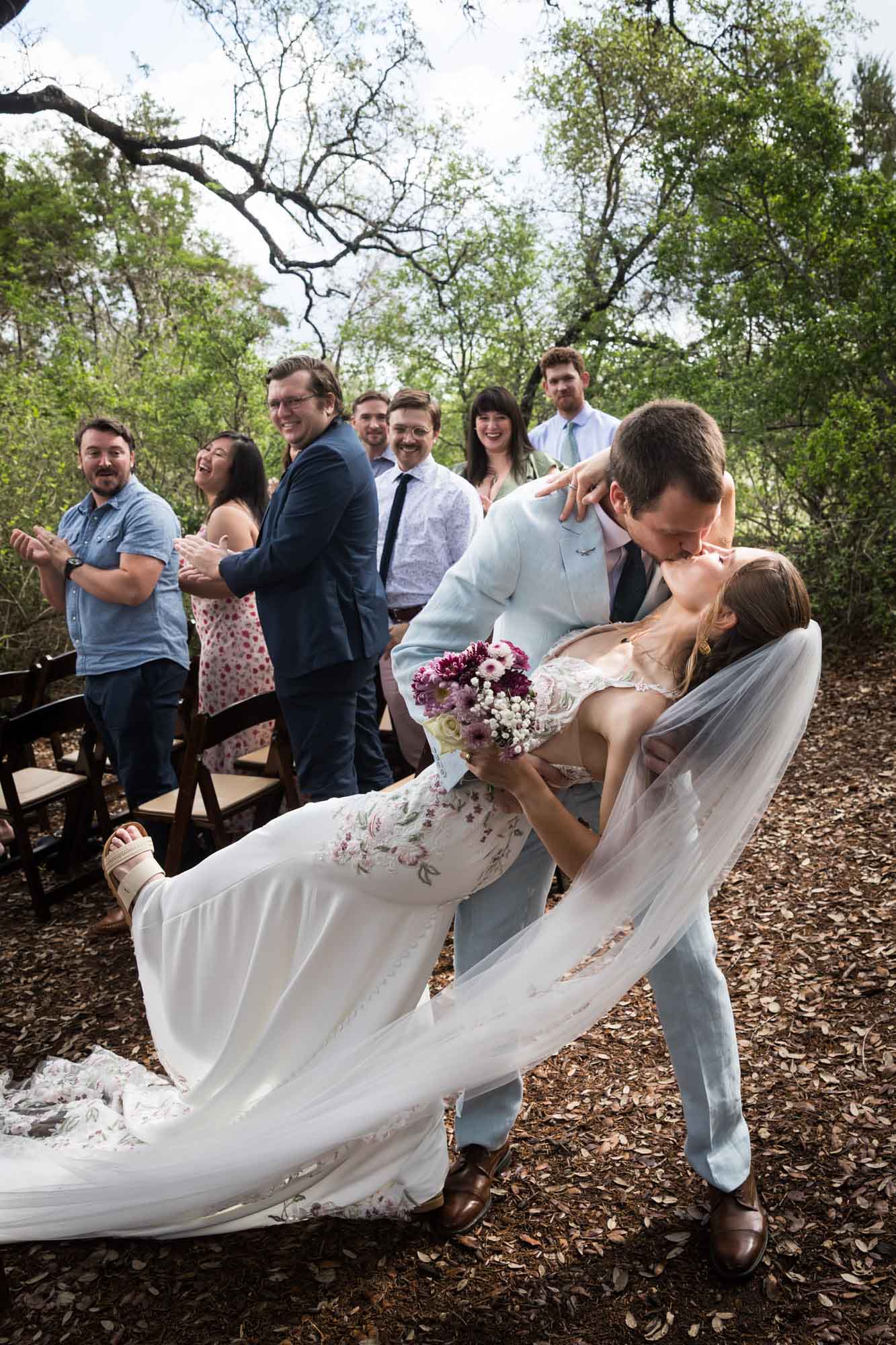 Bride and groom kissing with dramatic dip at end of aisle after ceremony during a Lady Bird Johnson Wildflower Center wedding