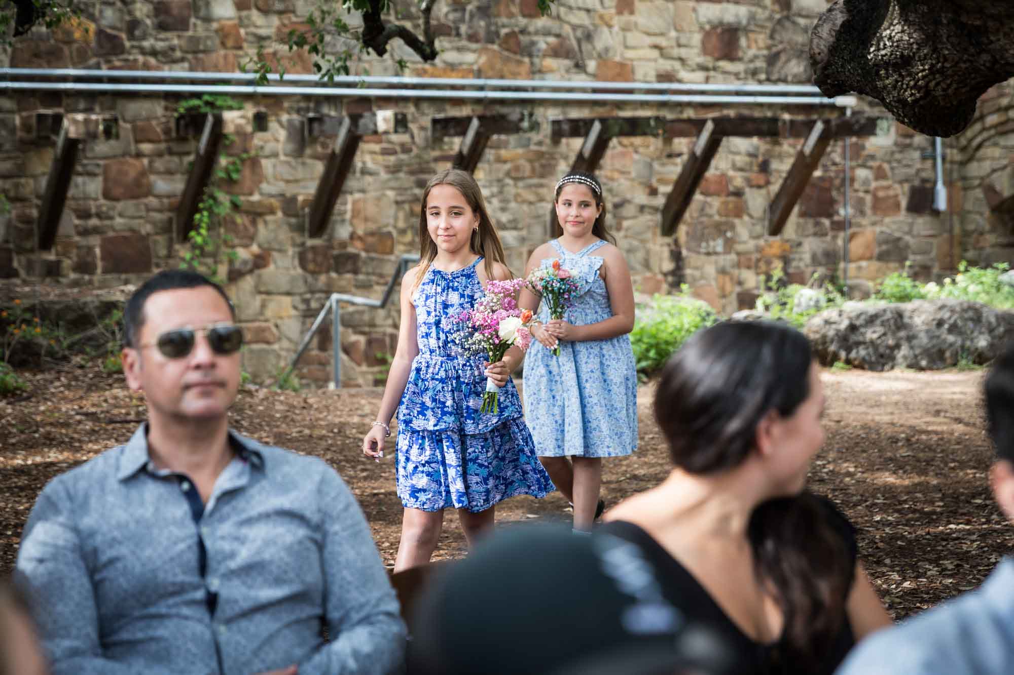Two little flower girls holding bouquets in front of guests during a Lady Bird Johnson Wildflower Center wedding