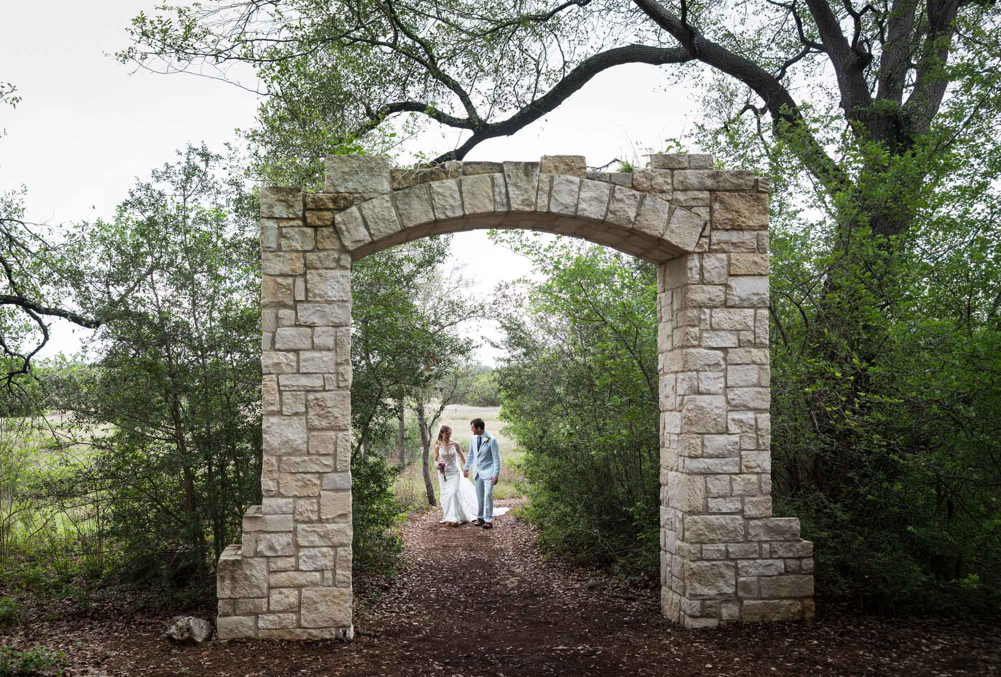 Lady Bird Johnson Wildflower Center wedding photos of a bride and groom walking down pathway through Cecille's Arch