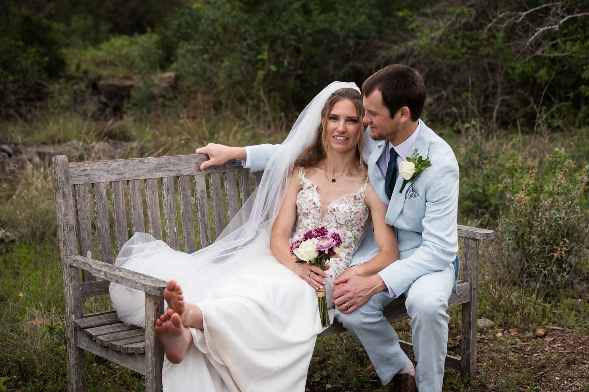 Lady Bird Johnson Wildflower Center wedding photos of a bride and groom seated on wooden bench in middle of Savanna Meadow