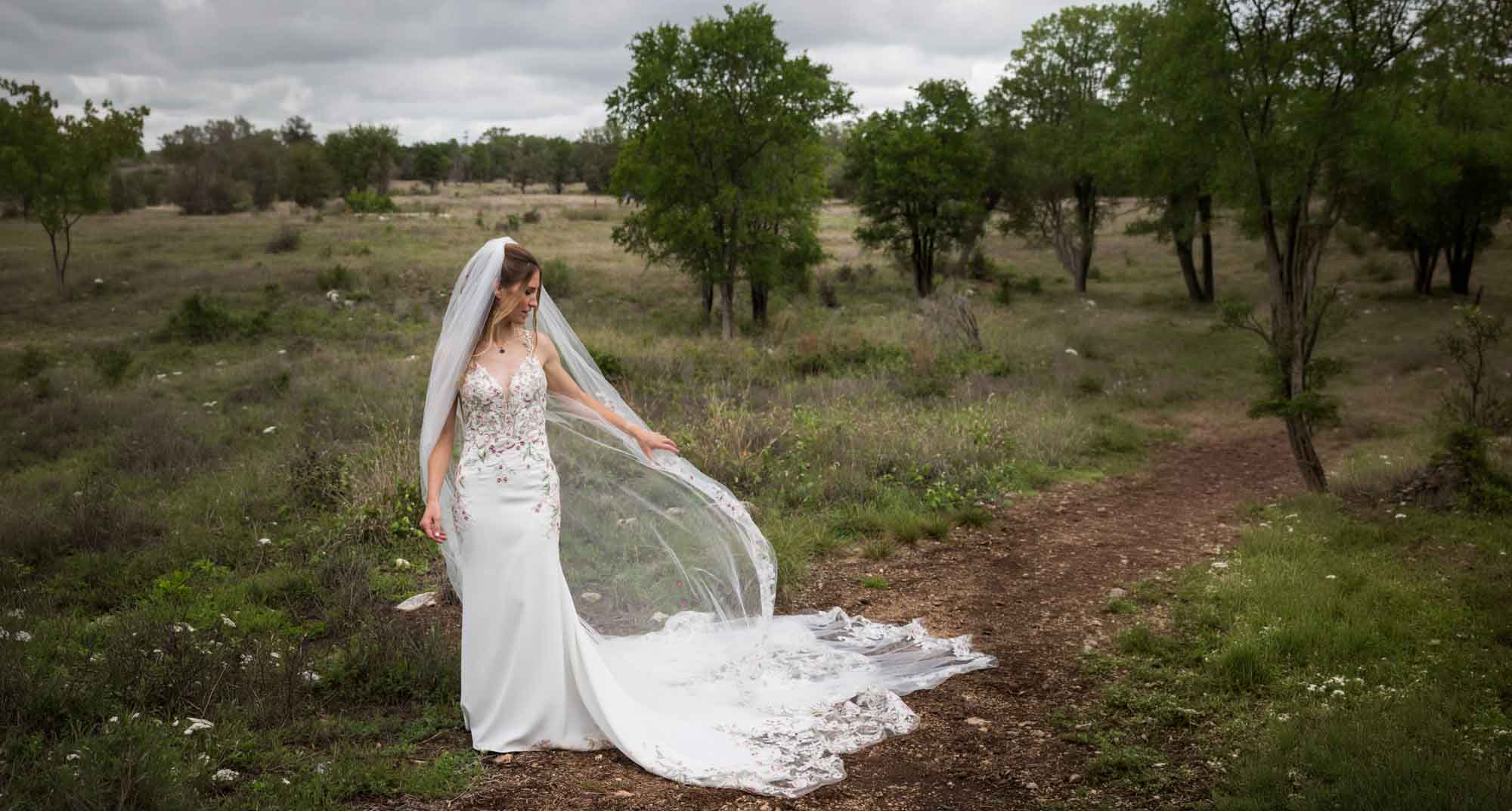 Lady Bird Johnson Wildflower Center wedding photos of a bride standing playing with long veil in middle of Savanna Meadow