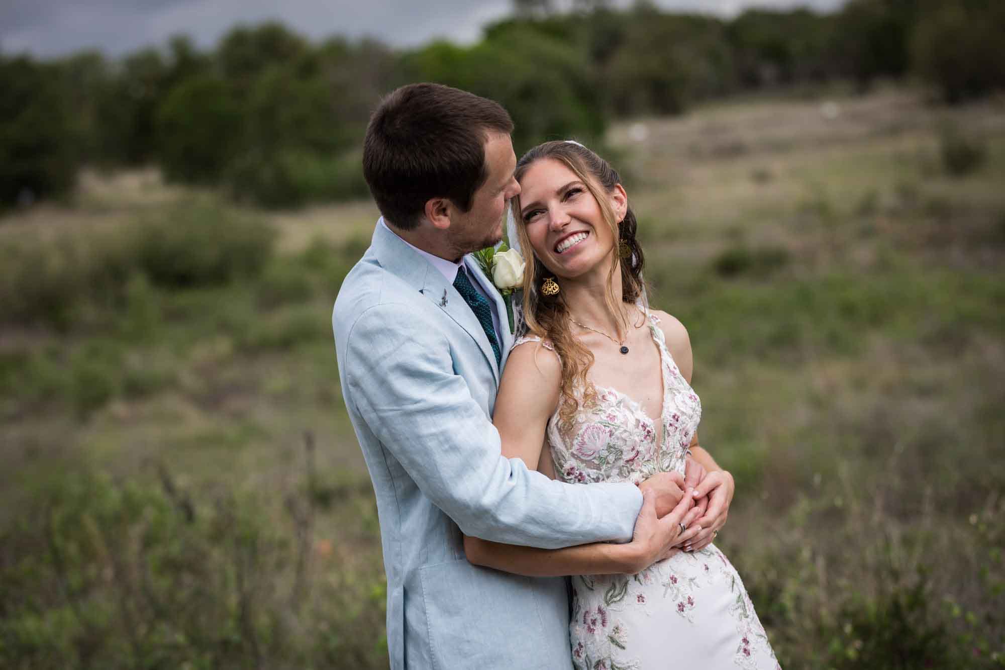 Lady Bird Johnson Wildflower Center wedding photos of a bride and groom hugging and laughing in middle of Savanna Meadow