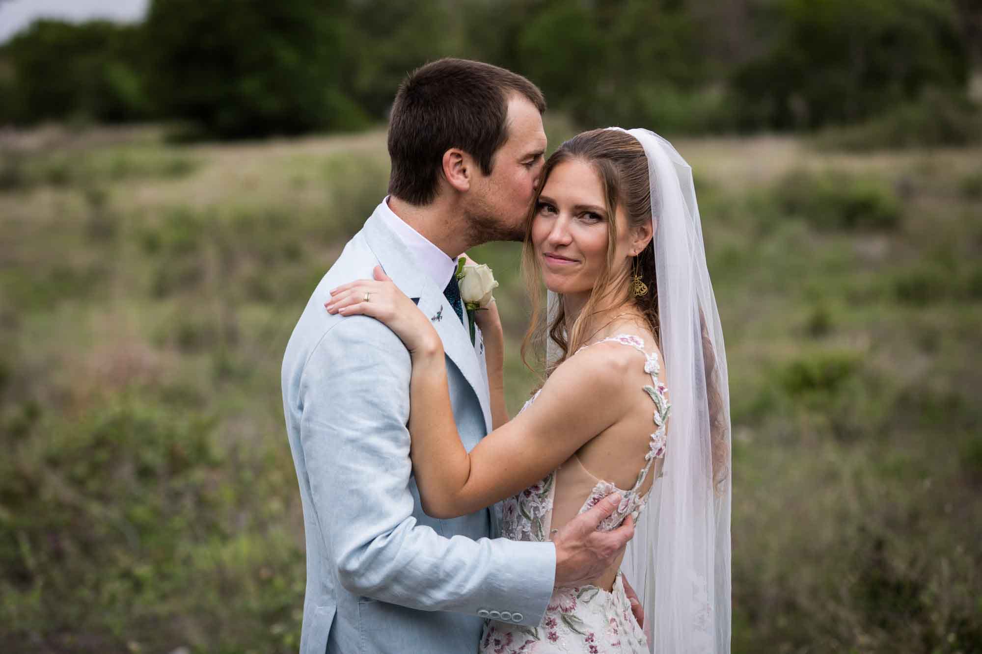 Lady Bird Johnson Wildflower Center wedding photos of a groom kissing bride on side of head in middle of Savanna Meadow