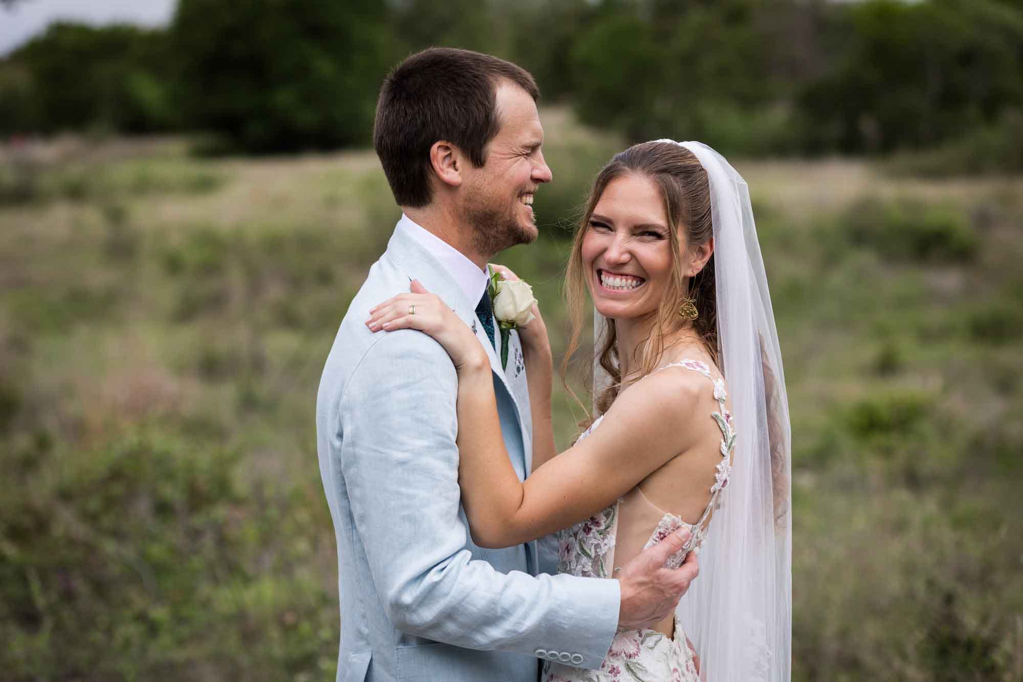 Lady Bird Johnson Wildflower Center wedding photos of a bride and groom hugging and laughing in middle of Savanna Meadow